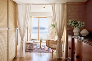 Een kamer met een houten vloer, een ronde tafel met stoelen, uitzicht op zee en een kastje met decoratieve spullen.