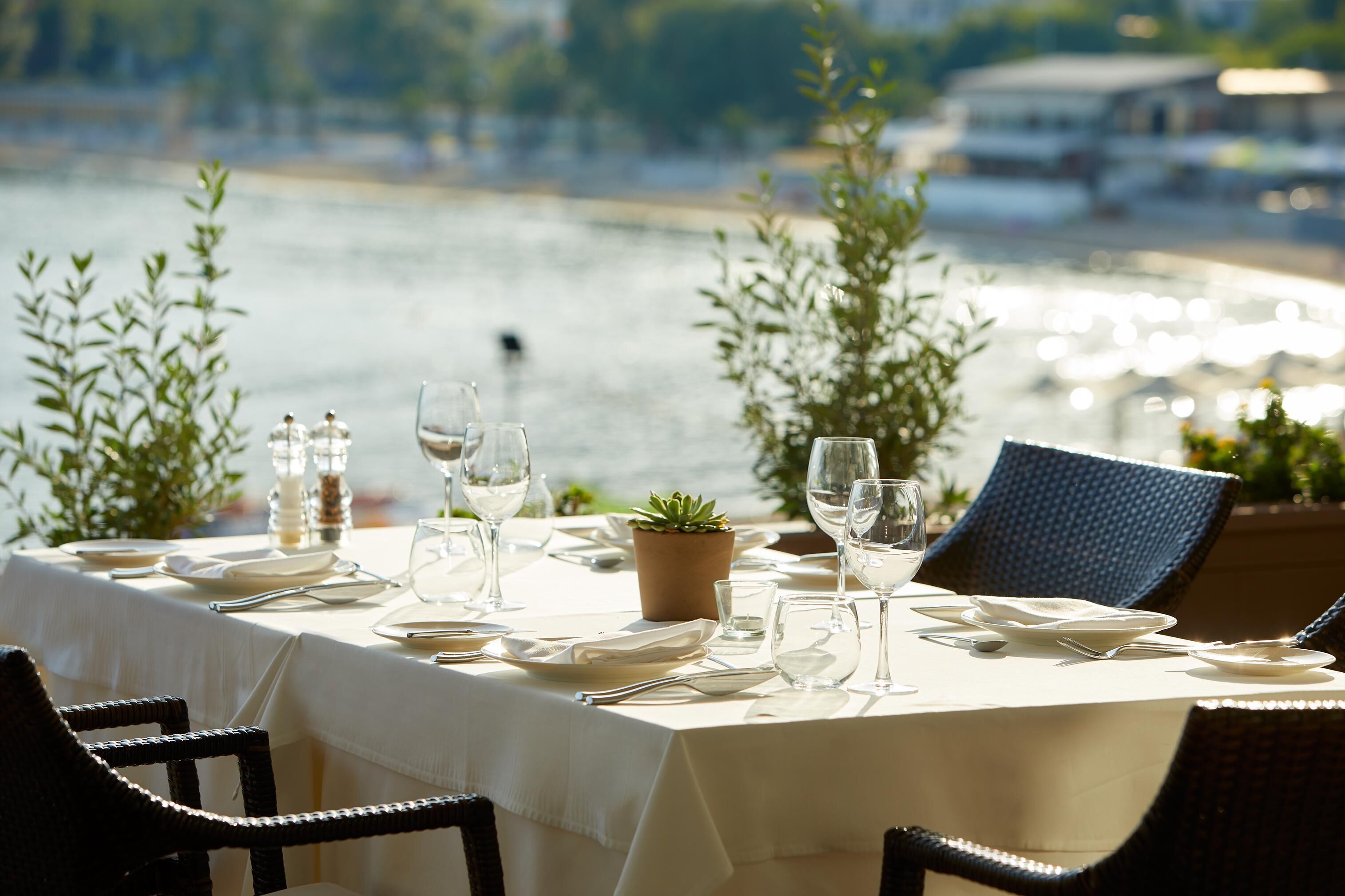 A table set for dining with a view of a body of water and boats in the background.