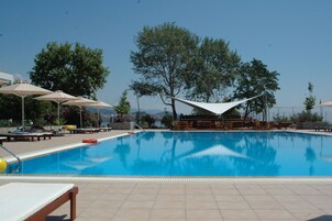 Una piscina con sillas de descanso y sombrillas, rodeada de árboles y con vistas a las montañas.