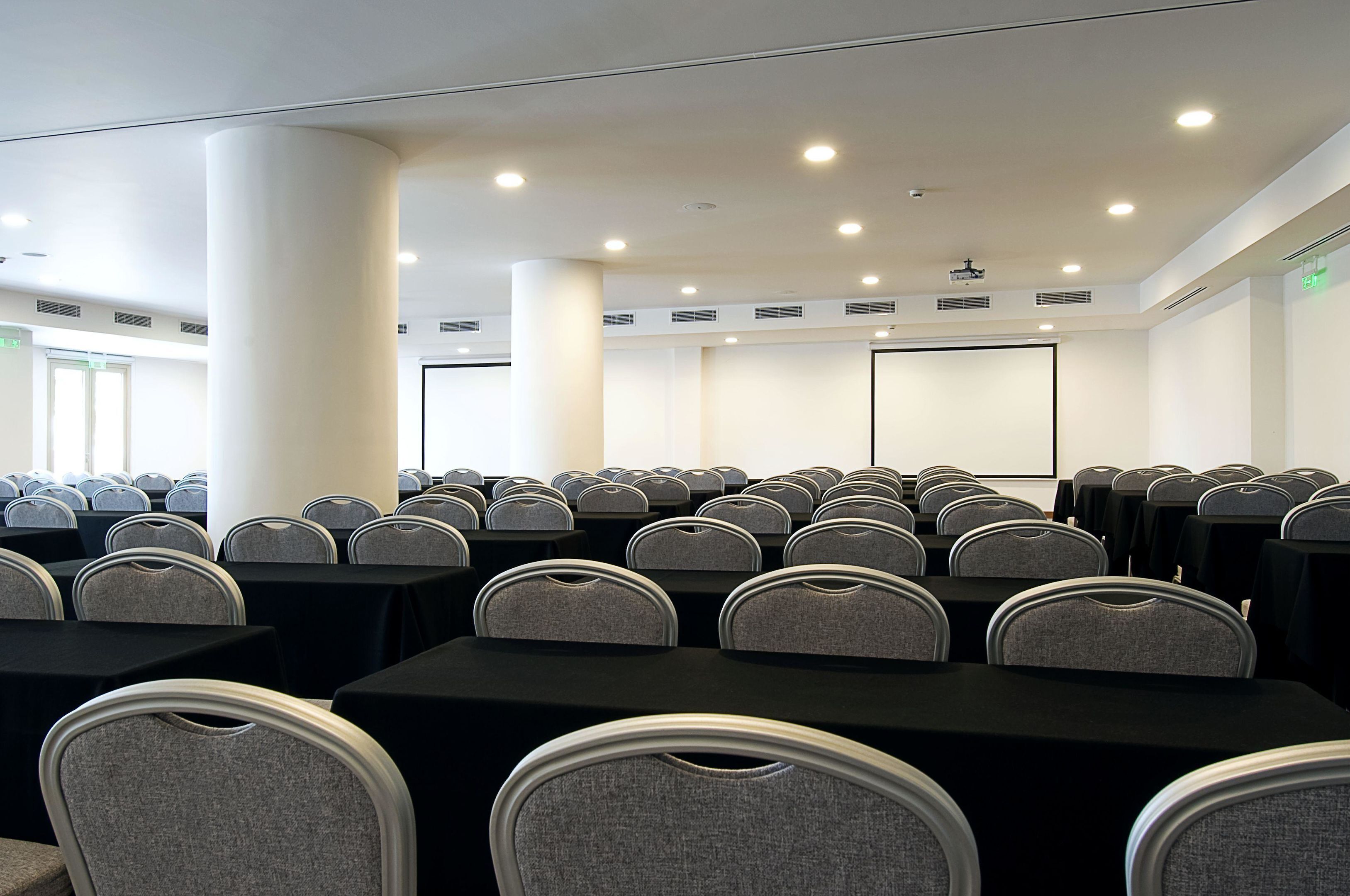 A conference room with rows of tables and chairs, a projector screen, and a whiteboard.