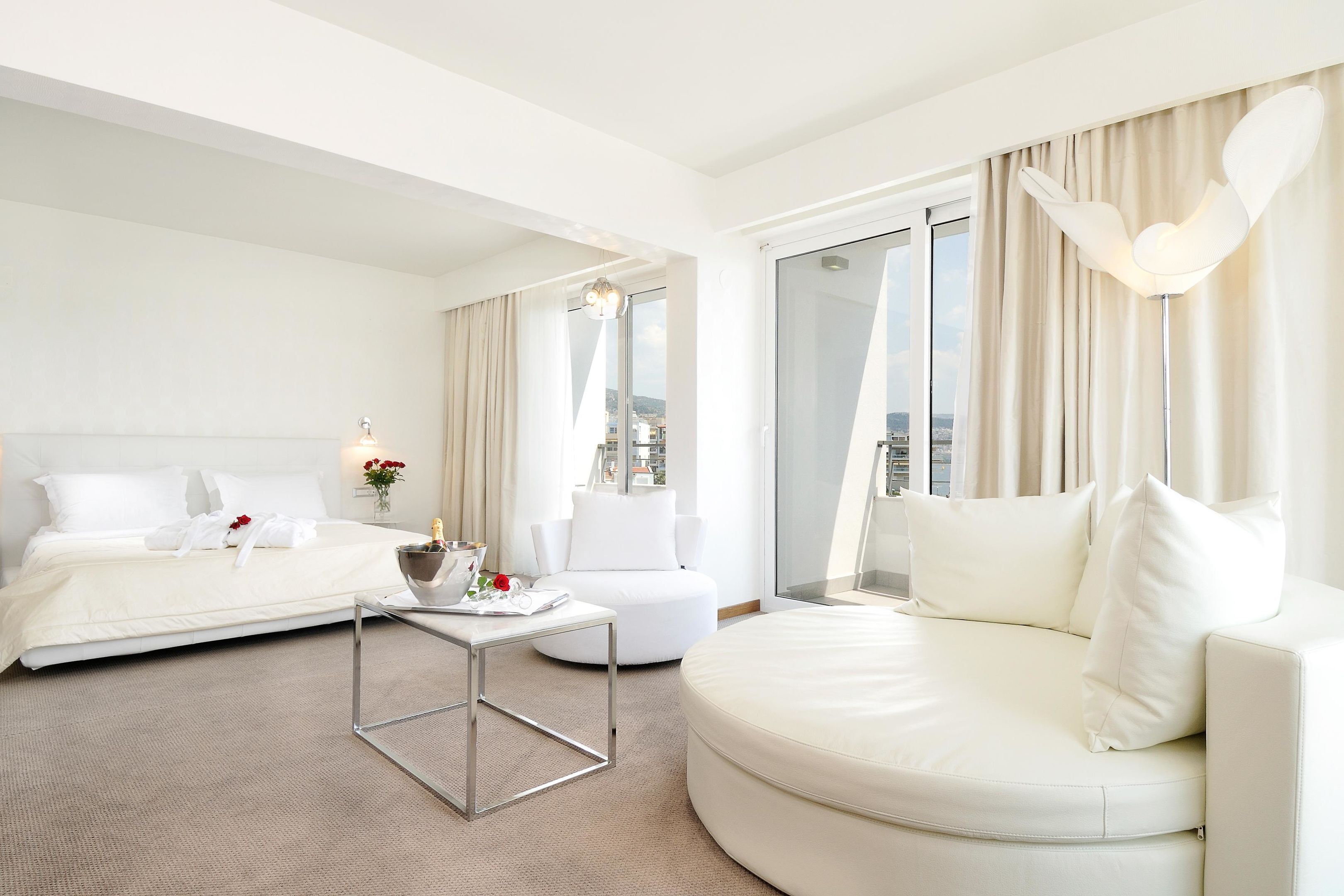 A hotel room with a bed, a sofa, a small table, and a view of the city through the window.