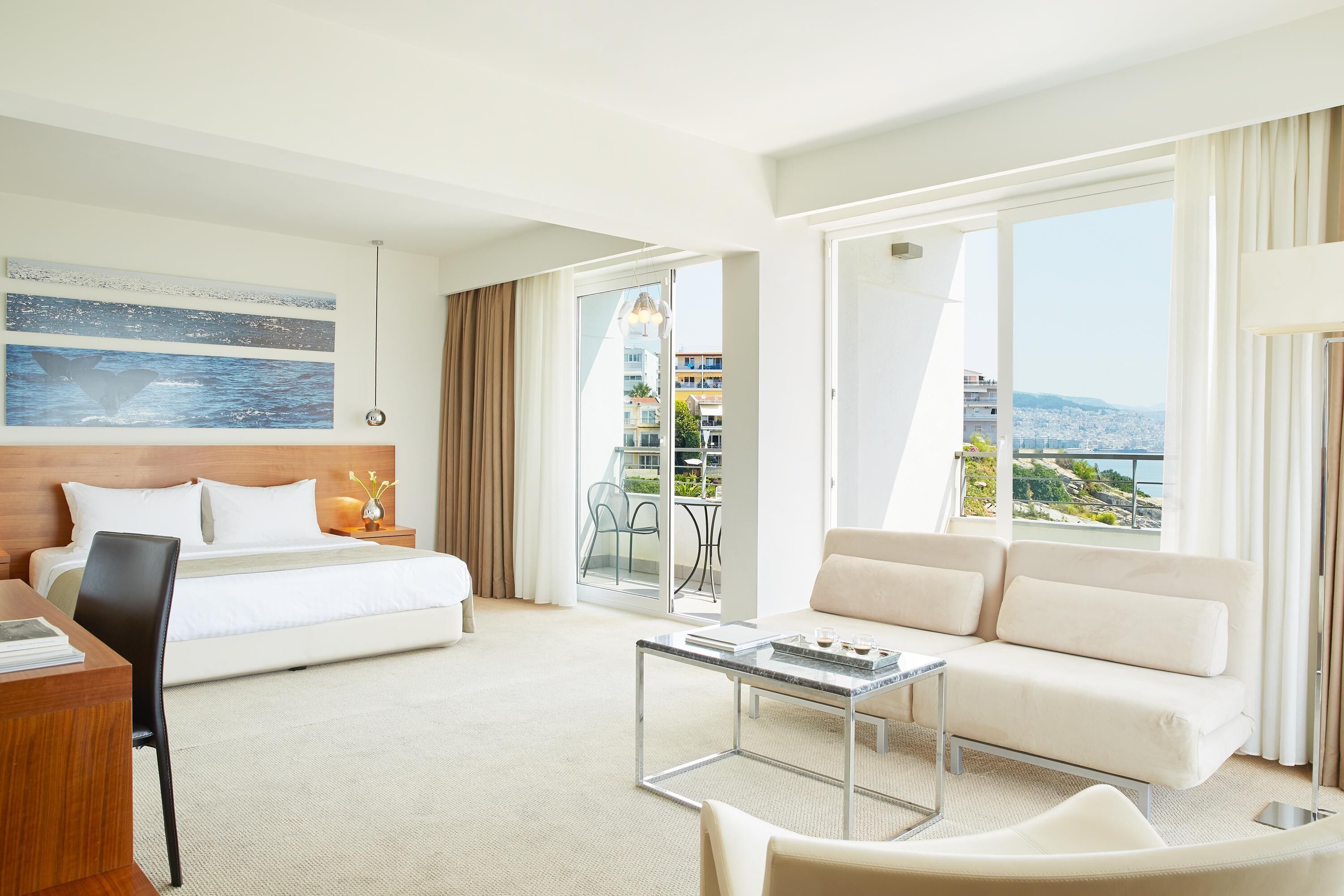 A hotel room with a bed, a sofa, a desk, and a balcony with a city view.