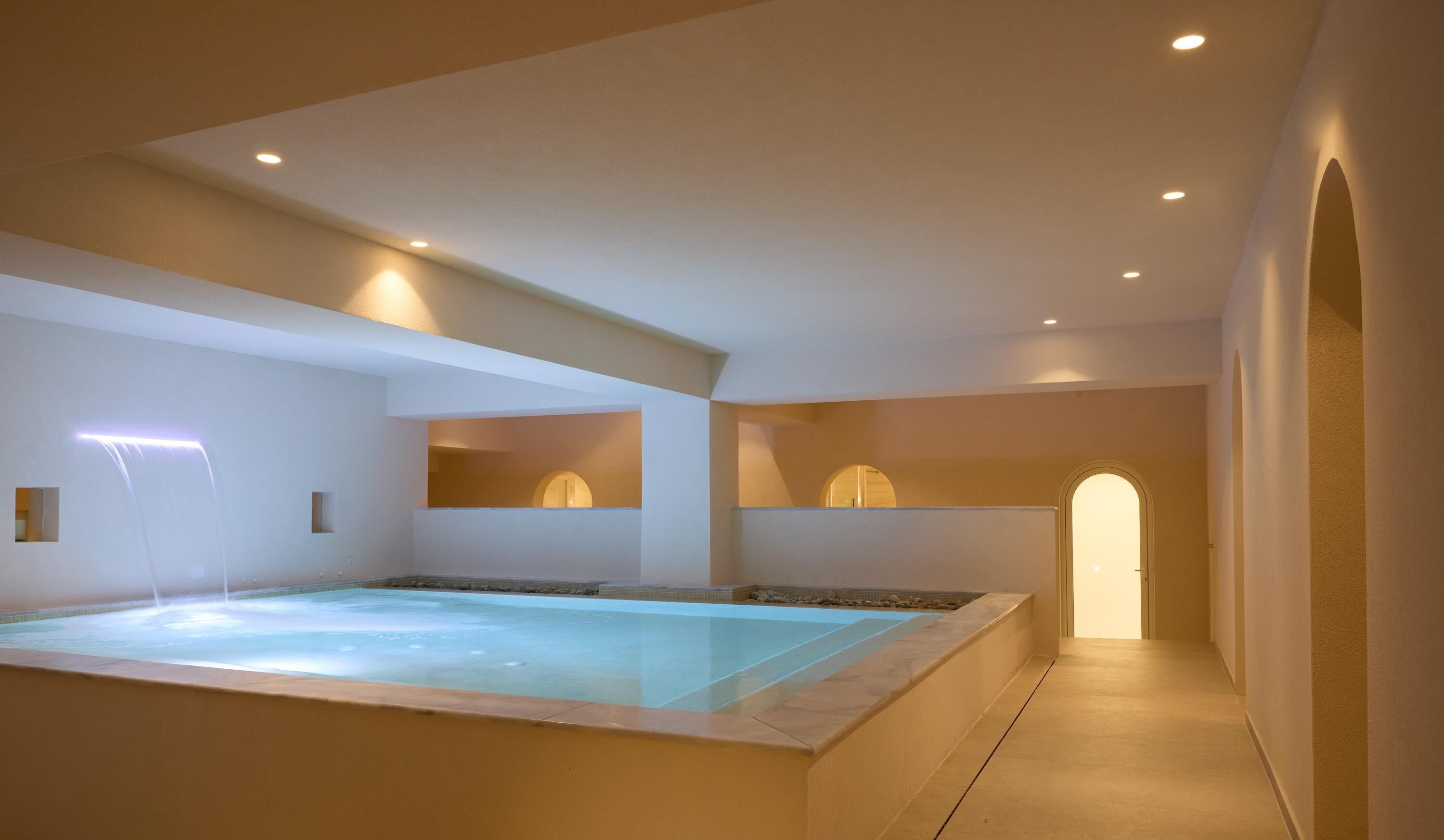 A spa area with a hot tub, a walk-in shower, and a corridor leading to an arched doorway.