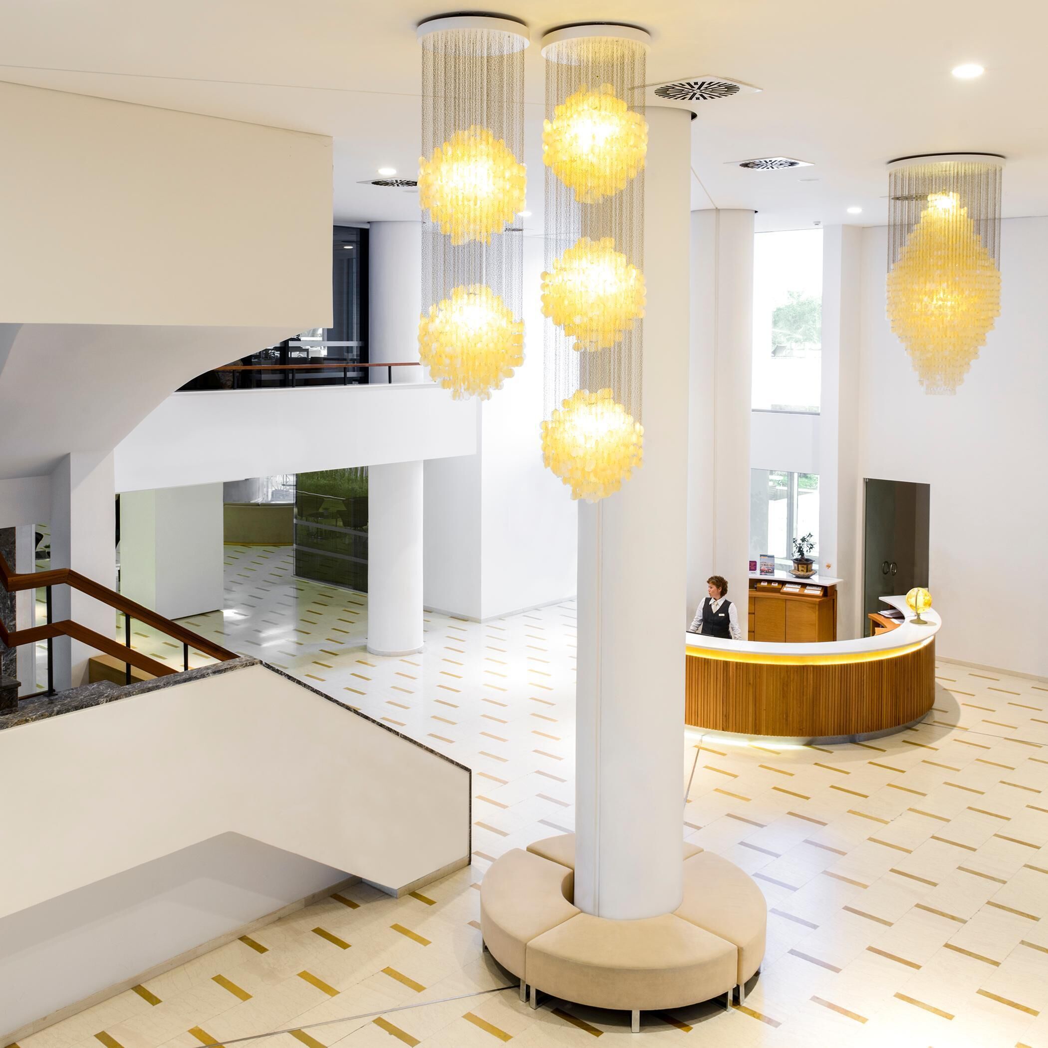 A modern lobby with a reception desk, a staircase, and multiple hanging chandeliers.