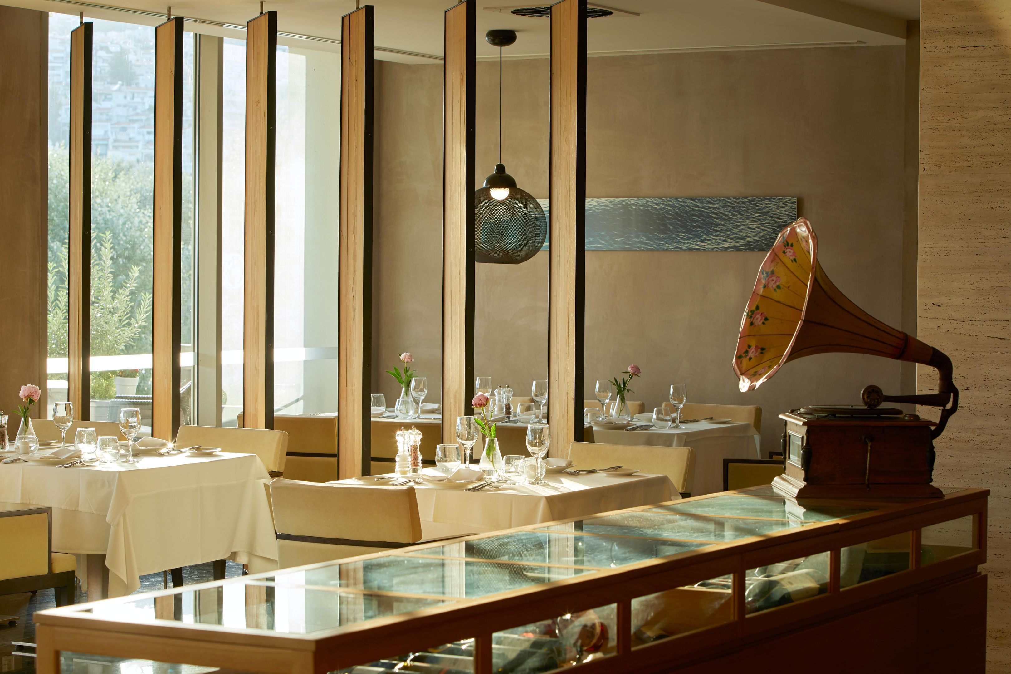 A restaurant with tables set for dining, a gramophone, and large windows allowing natural light.