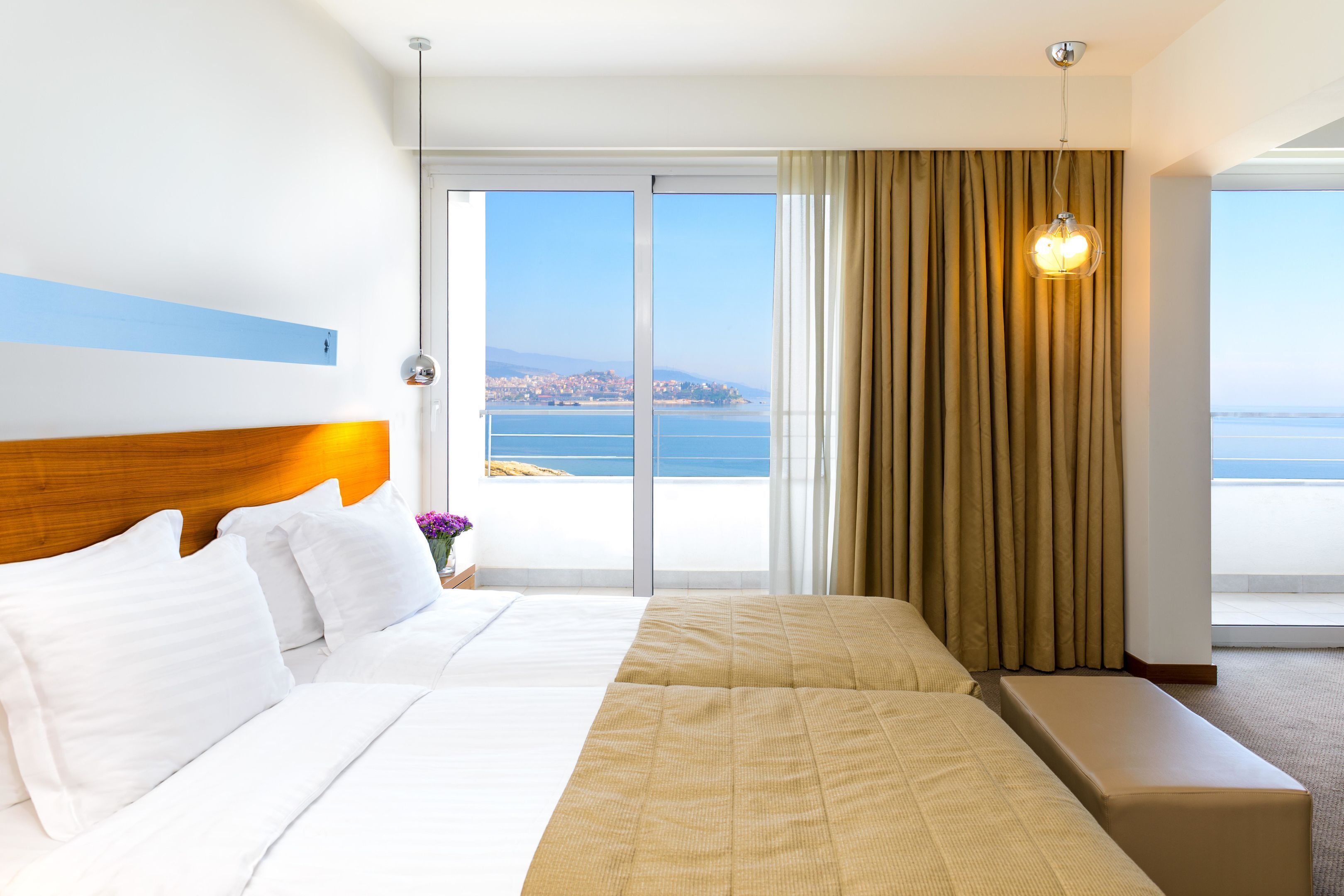 A hotel room with a large bed, a bench, a view of the sea, and a curtain.