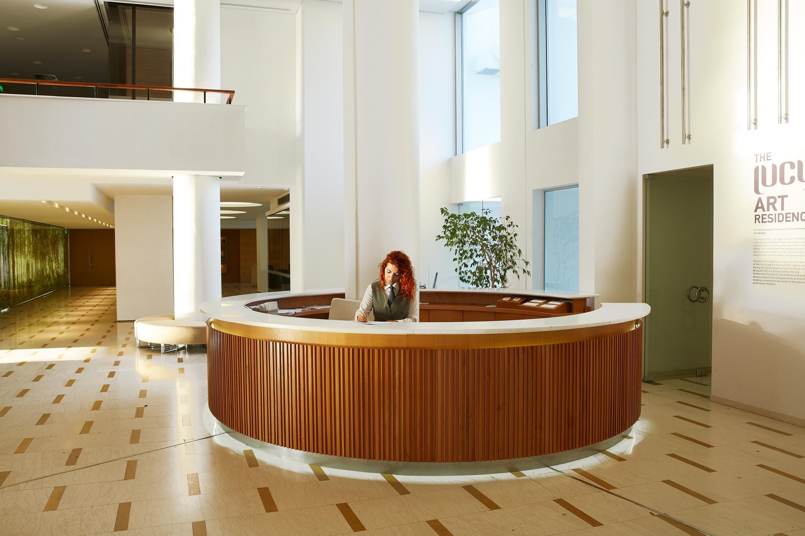 A reception area with a wooden reception desk, a potted plant, and a large window.