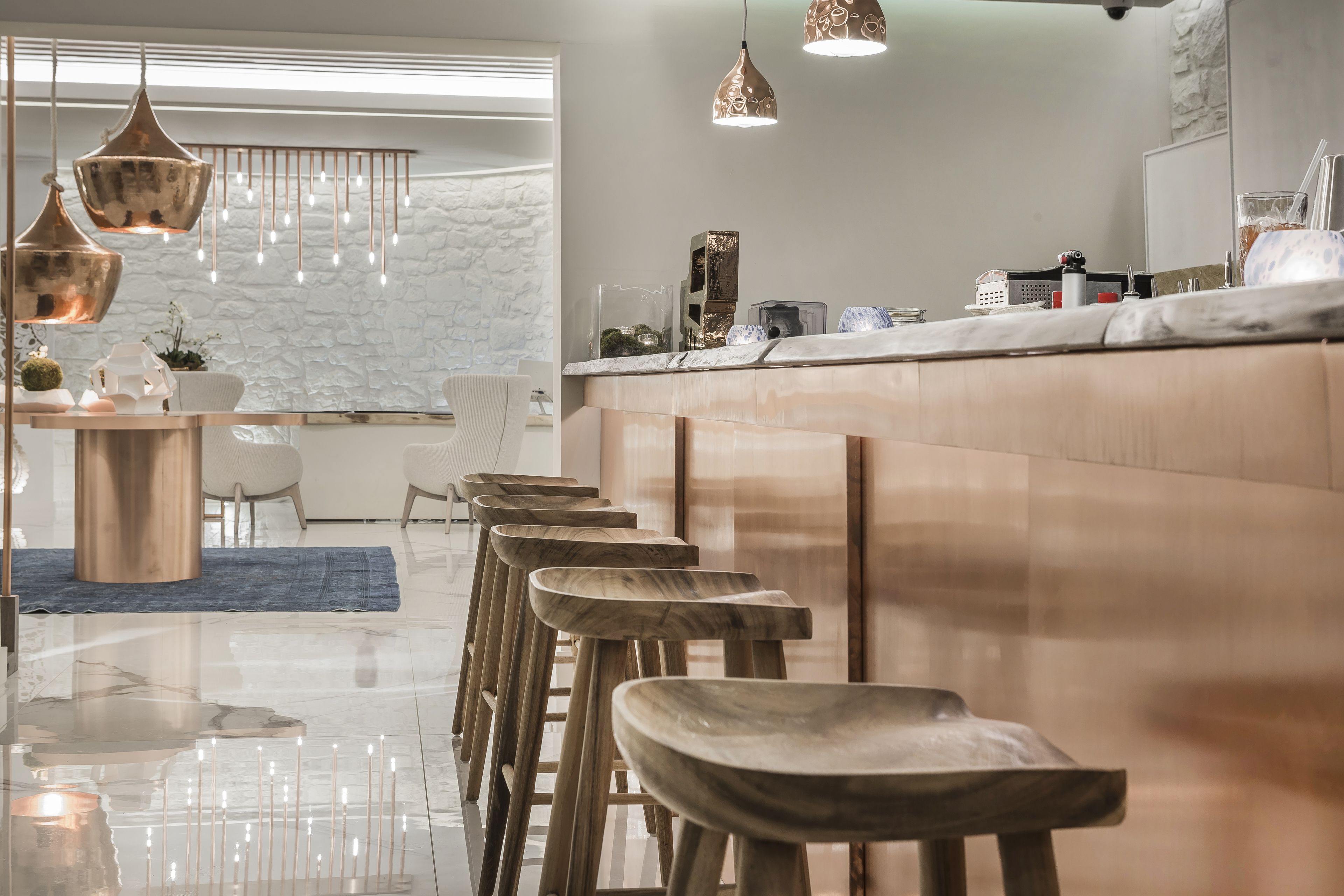 A modern bar area with wooden stools, hanging pendant lights, and a marble countertop.