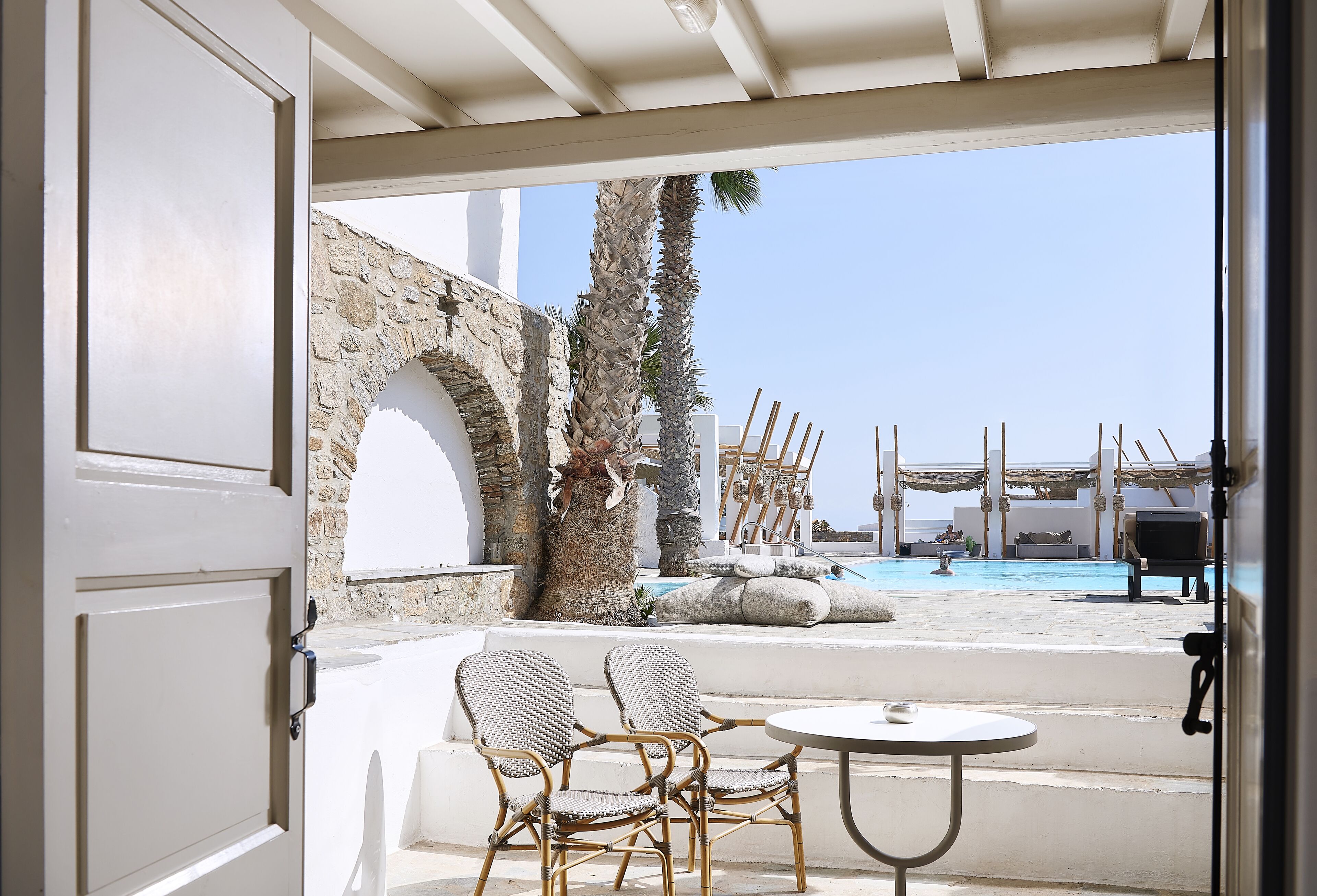 An outdoor seating area with wicker chairs and a small table, overlooking a pool and a stone wall.