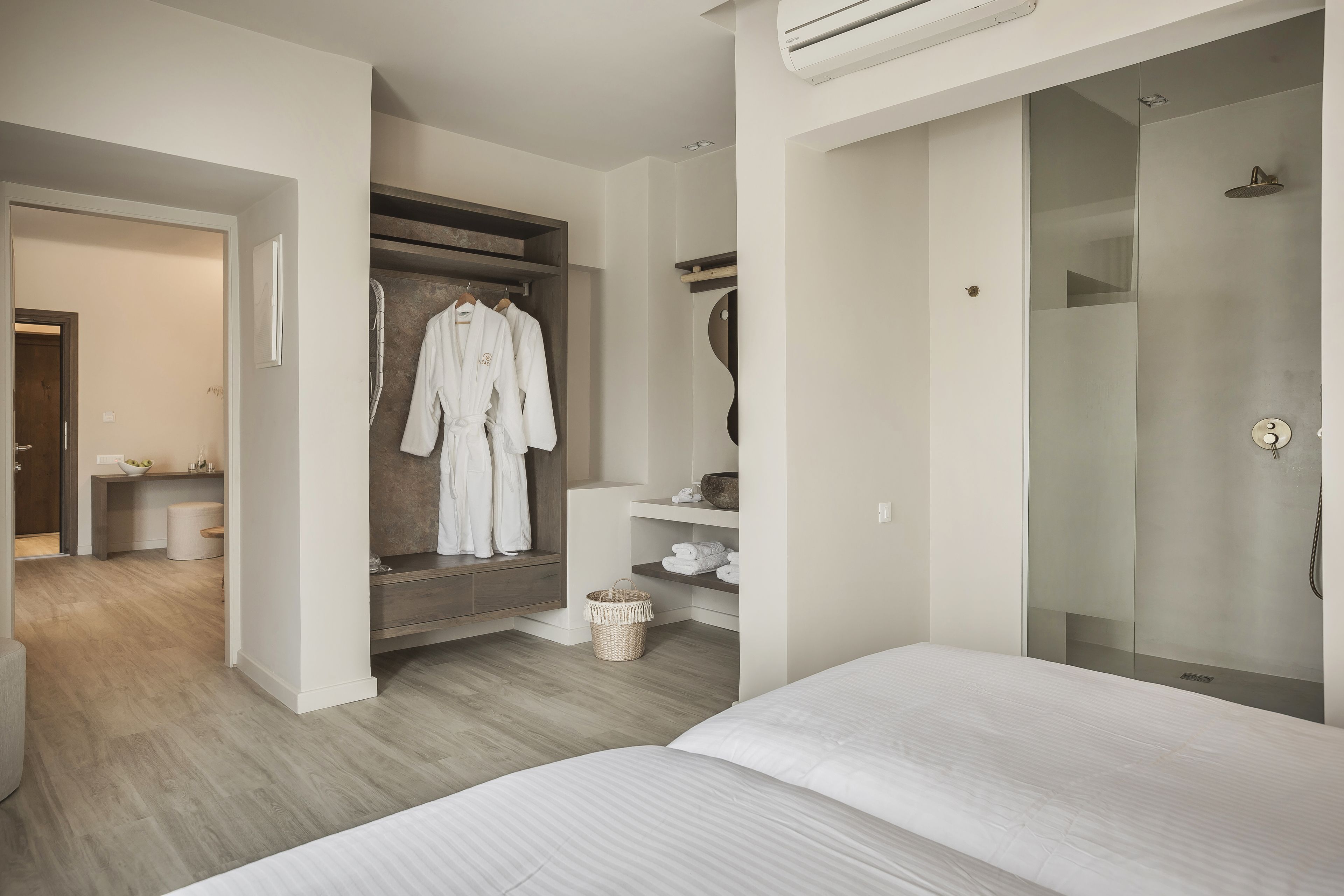 A modern bedroom with a large bed, a walk-in closet, and a shower area.