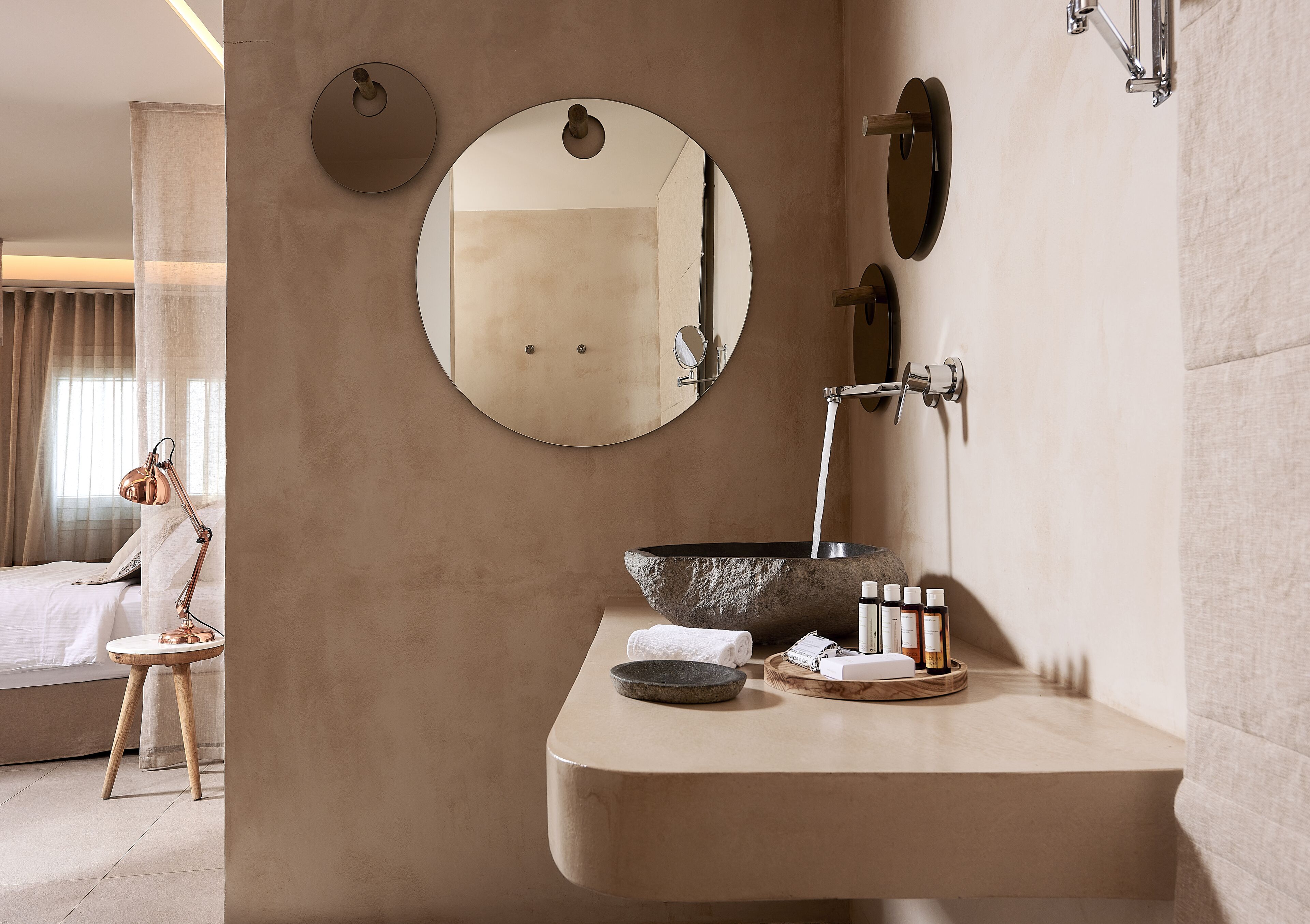 A bathroom with a large mirror, a stone basin, and toiletries on a wooden tray.