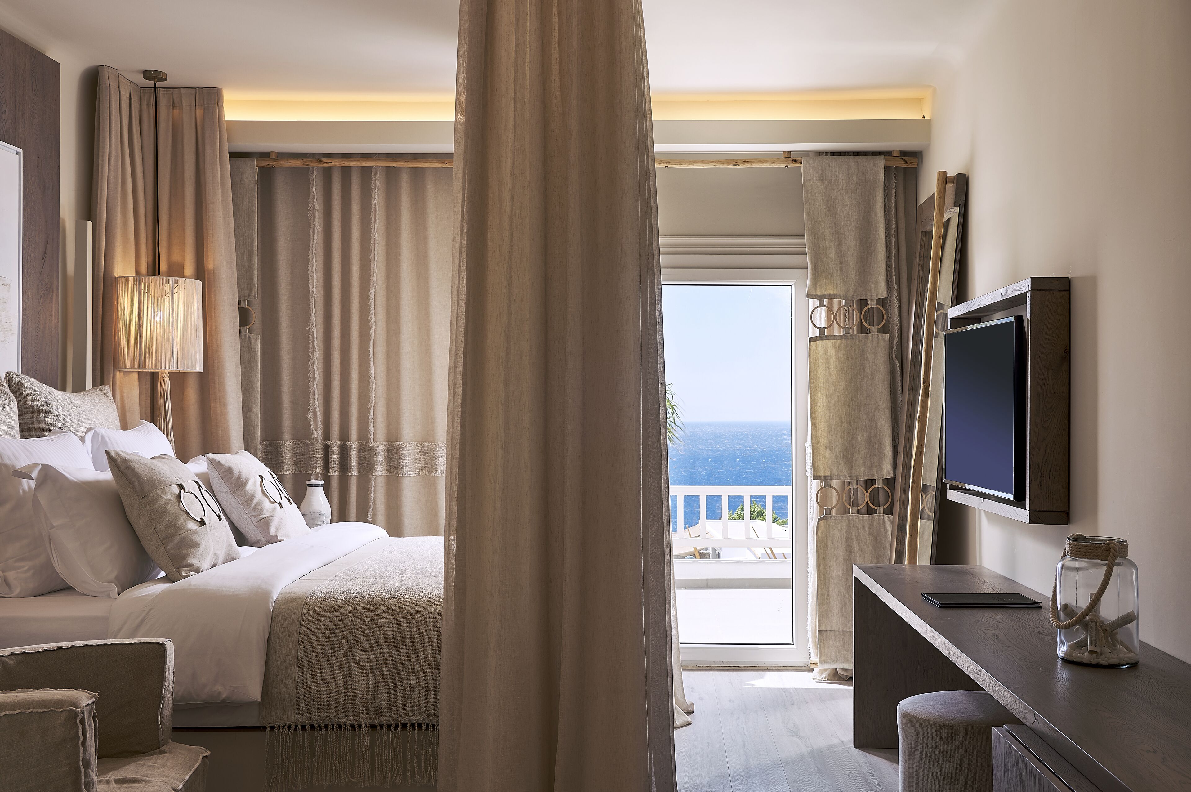 A hotel room with a bed, a desk, a TV, and a view of the ocean.