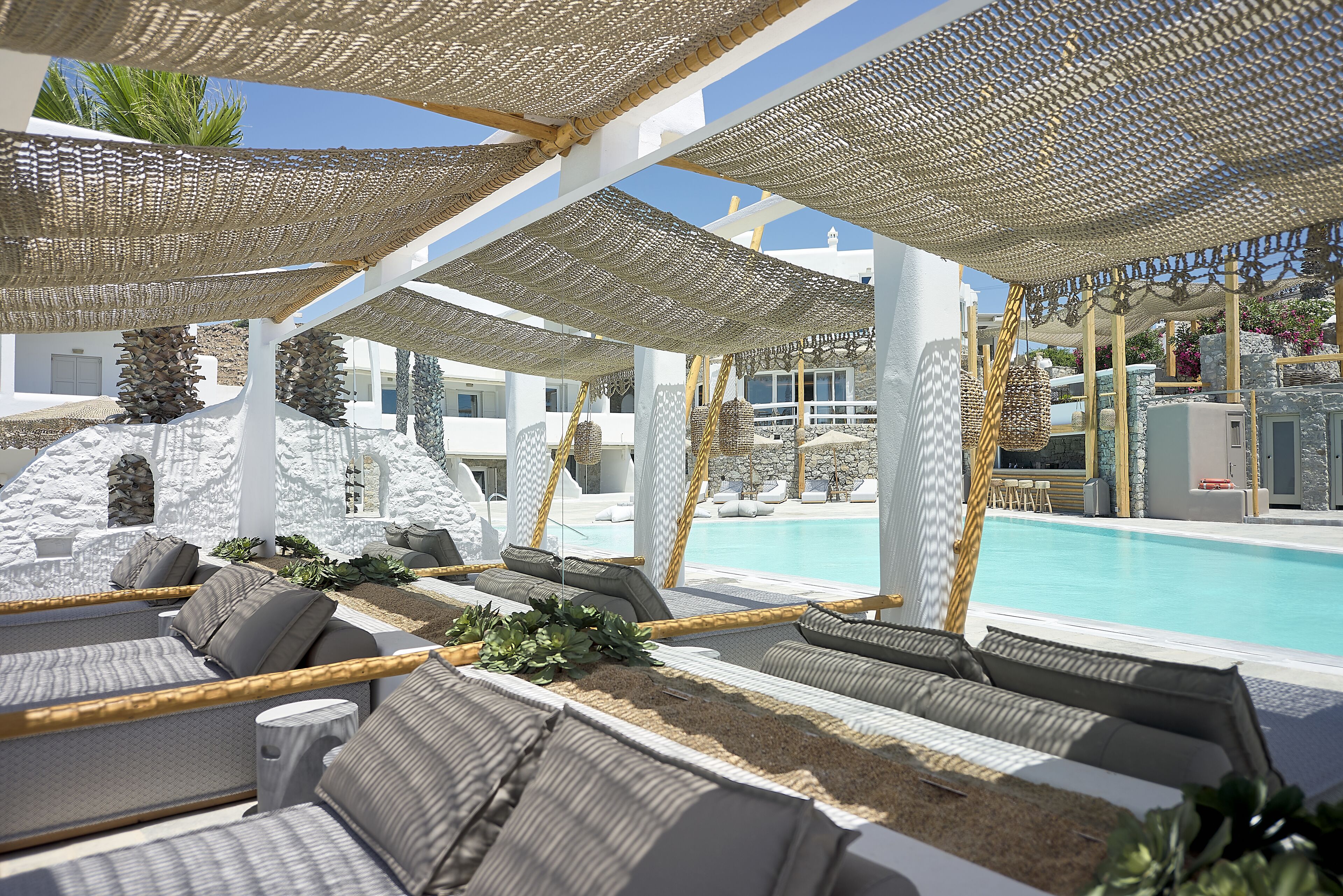 A poolside lounge area with sun loungers, a pool, and a white building in the background.