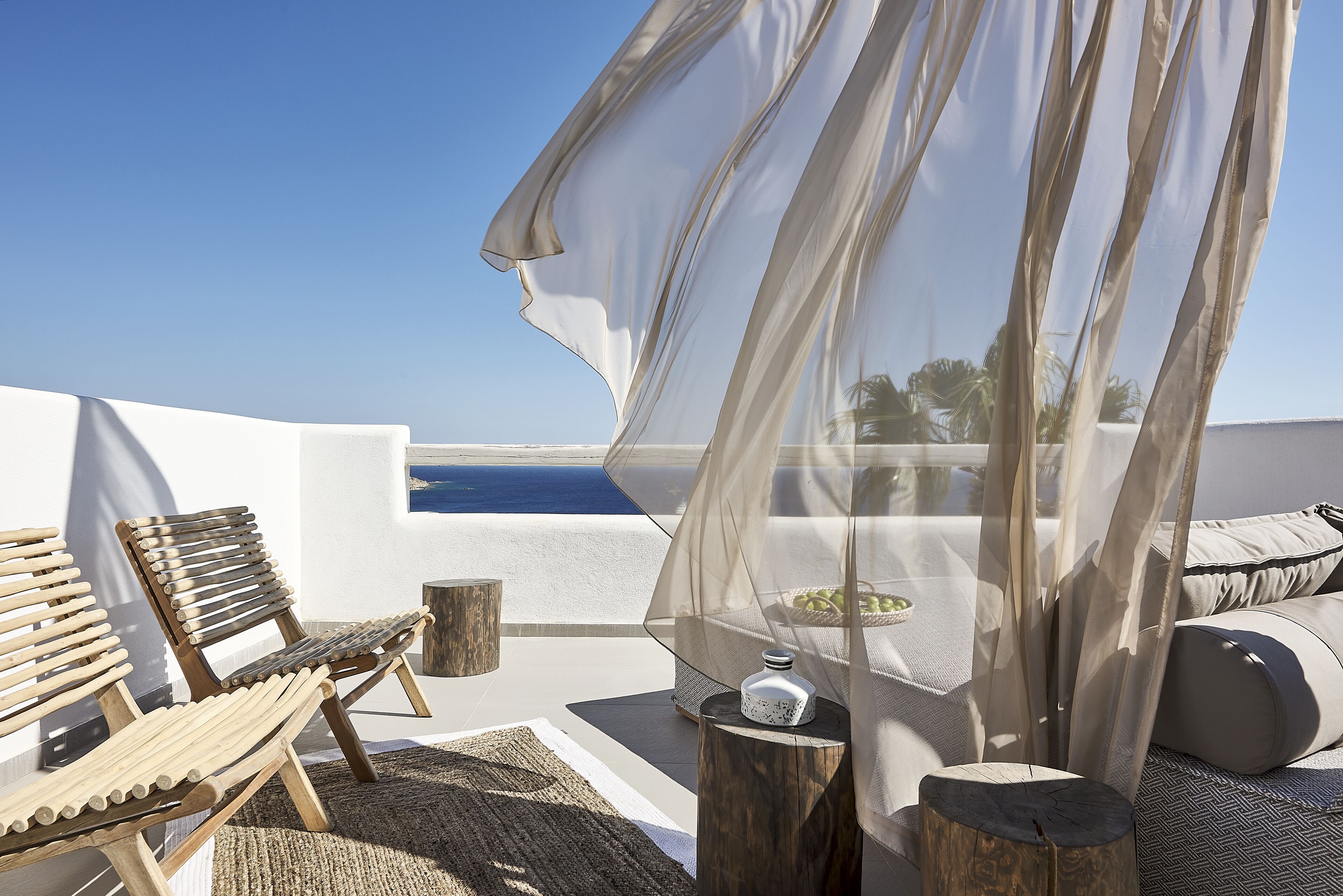 A terrace with wooden chairs, a table with a bottle, and a view of the sea.