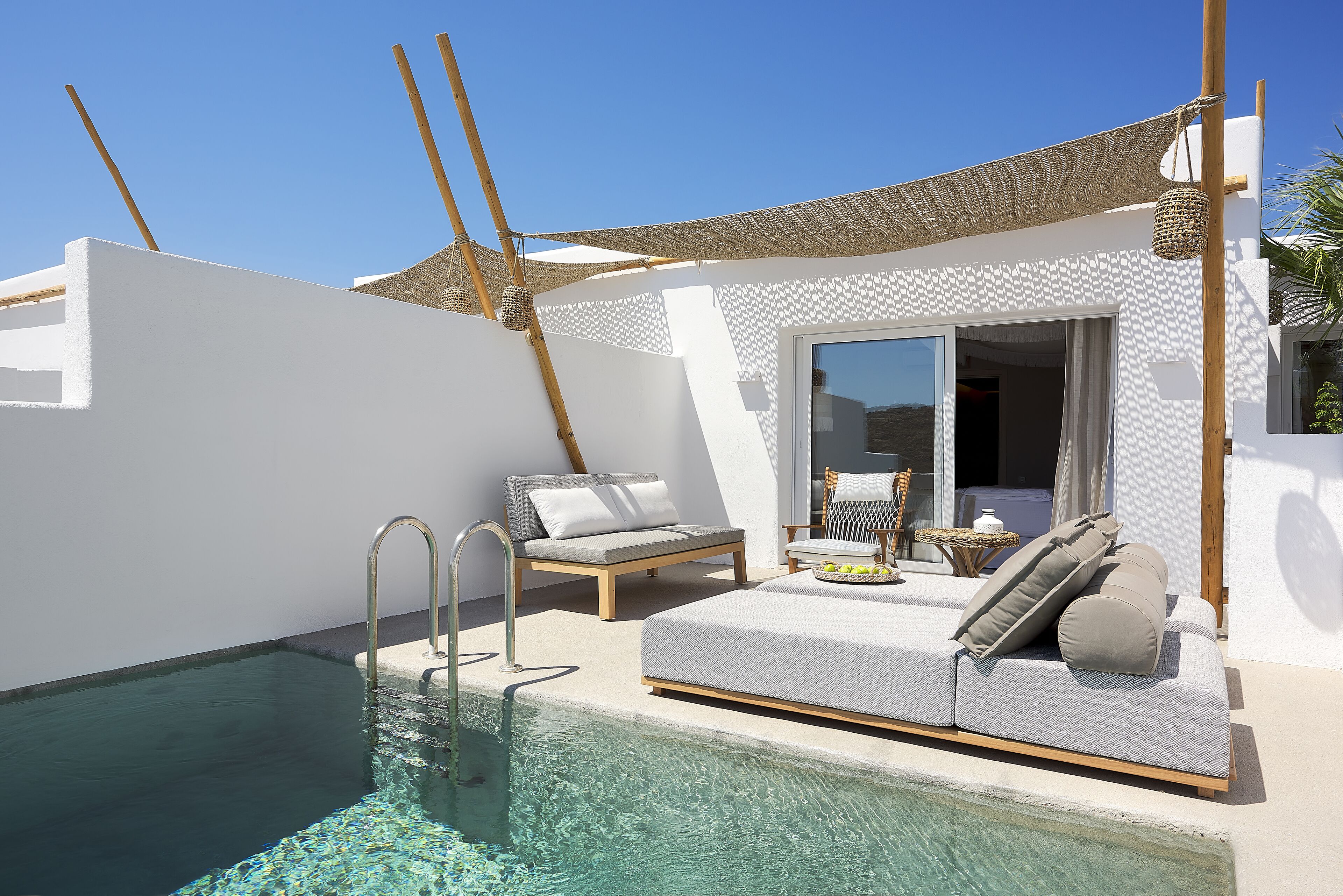 Un espace aménagé au bord de la piscine, comprenant un fauteuil de relaxation, un canapé et une petite table sur laquelle est disposé un plateau de fruits.