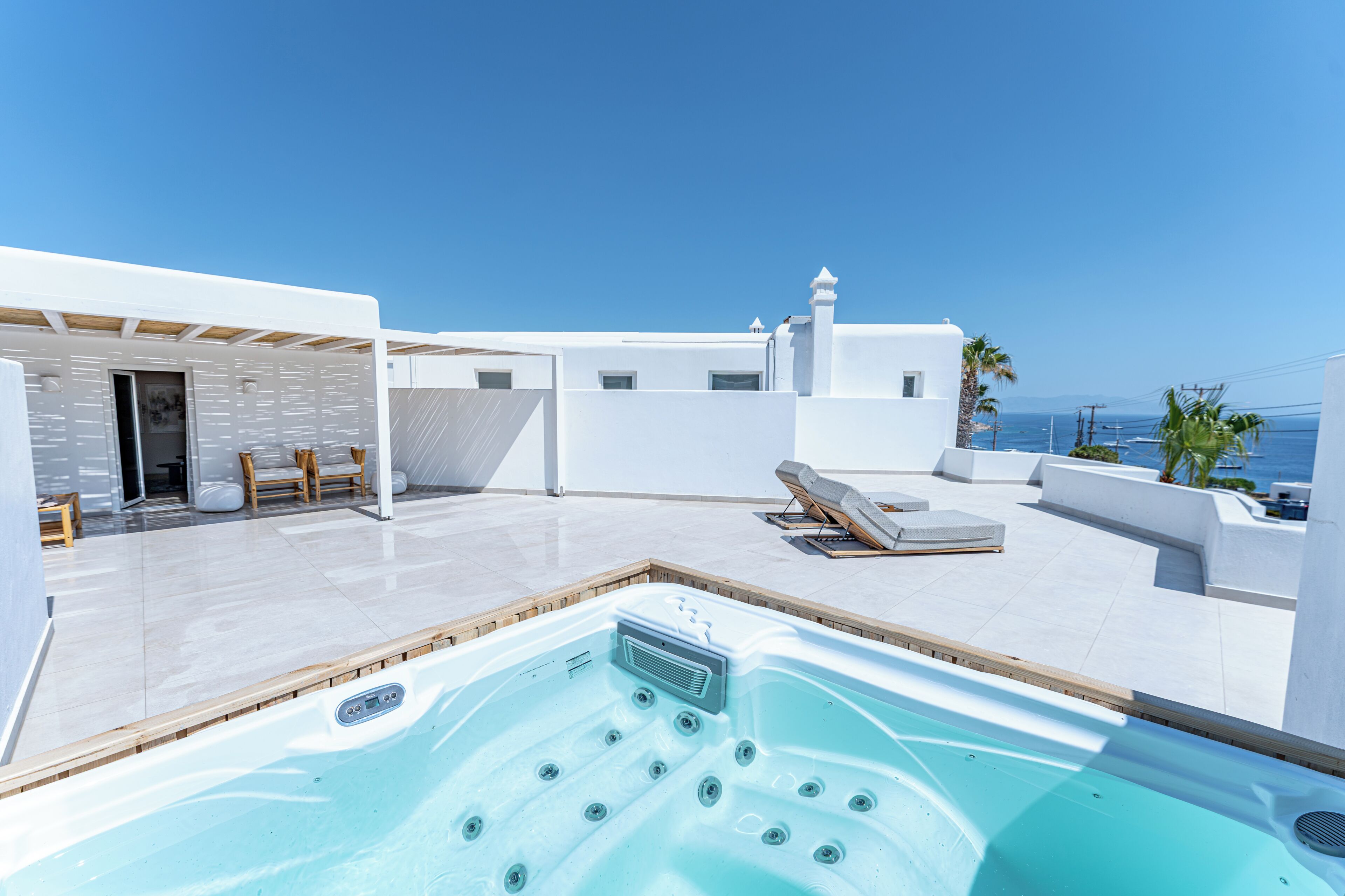 A rooftop terrace with a hot tub, lounge chairs, and a view of the sea.