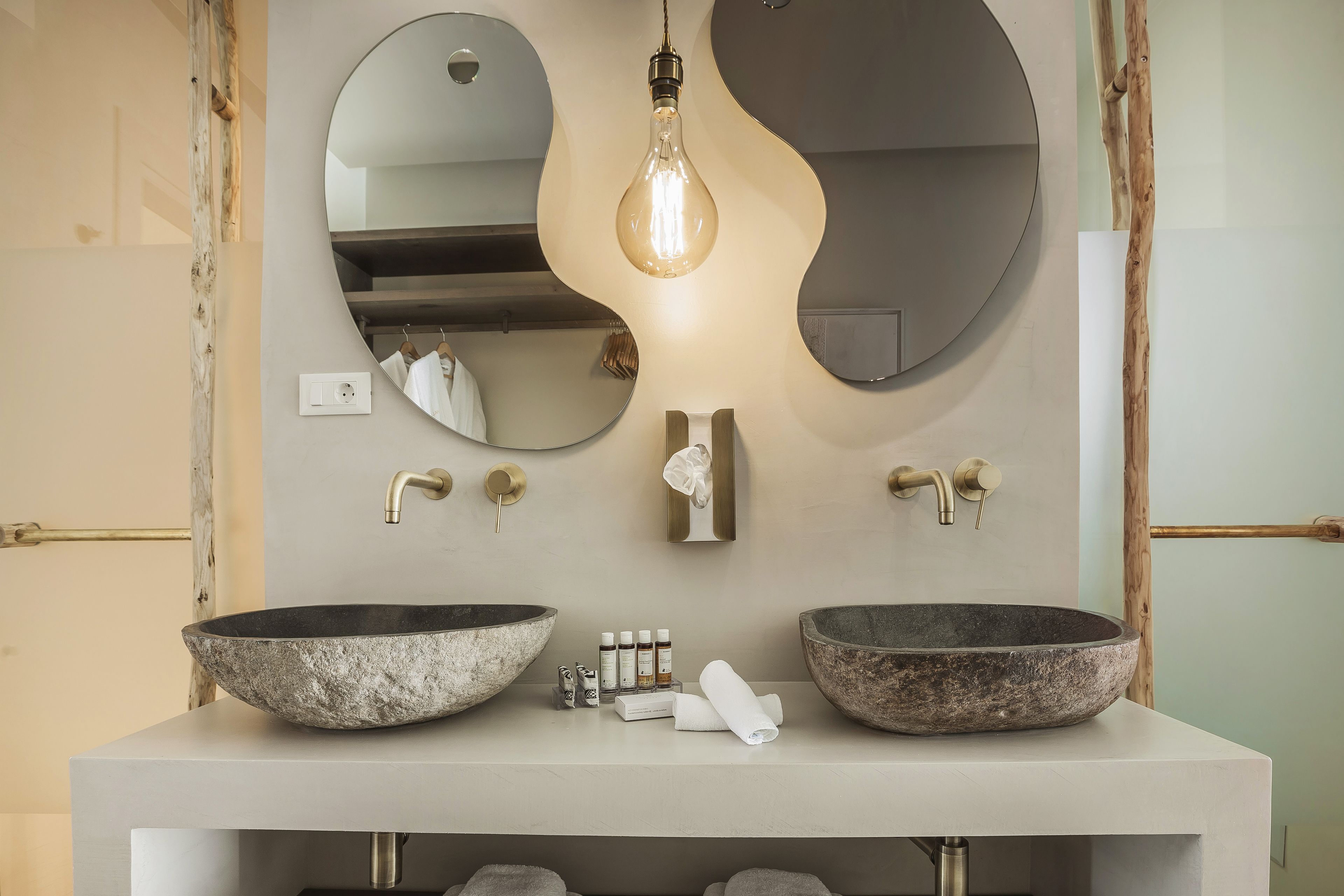 A bathroom with two large stone sinks, a light bulb, and a mirror with a unique wavy design.