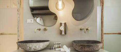 A bathroom with two large stone sinks, a light bulb, and a mirror with a unique wavy design.