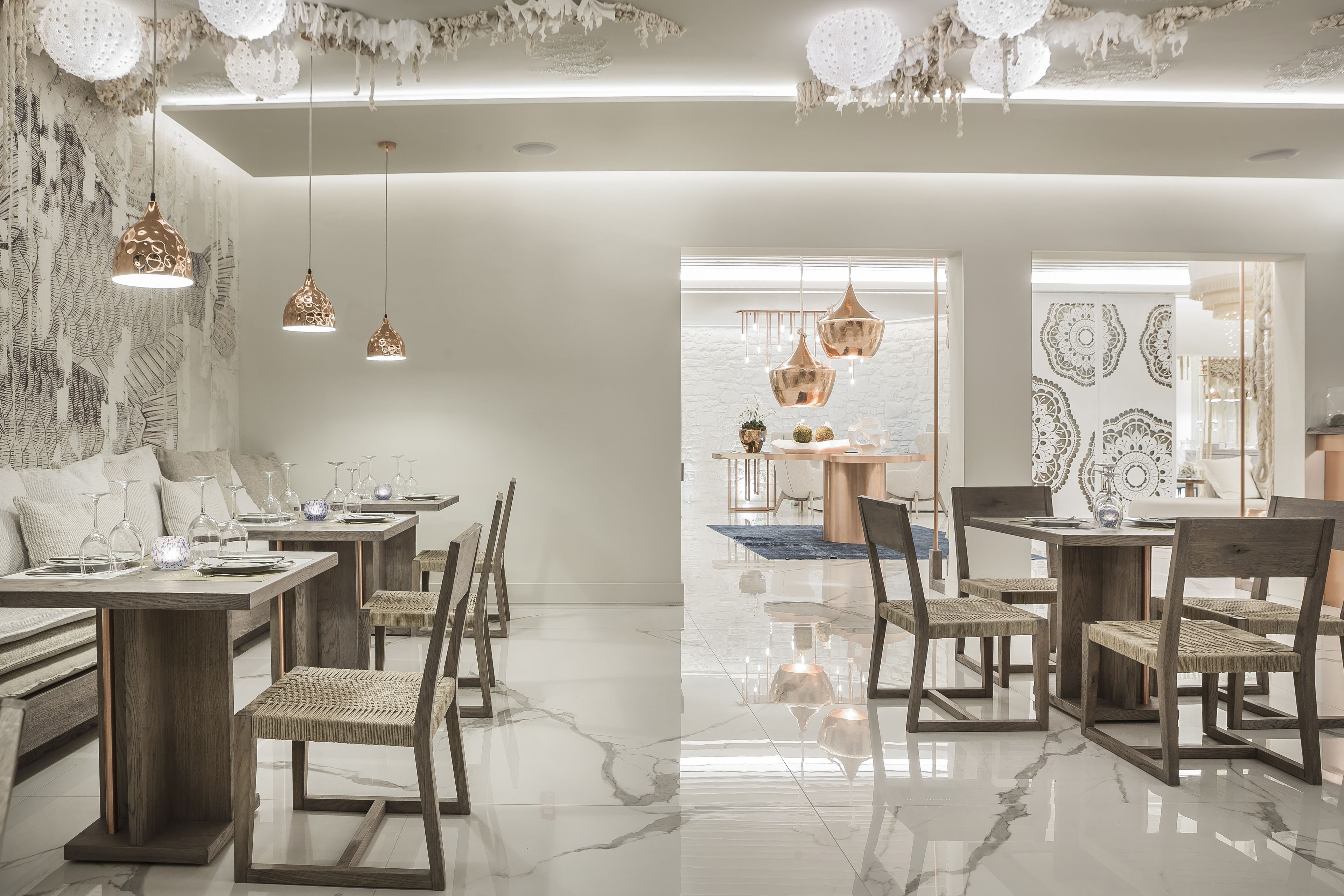 A modern dining area with wooden tables and chairs, hanging pendant lights, and a marble floor.