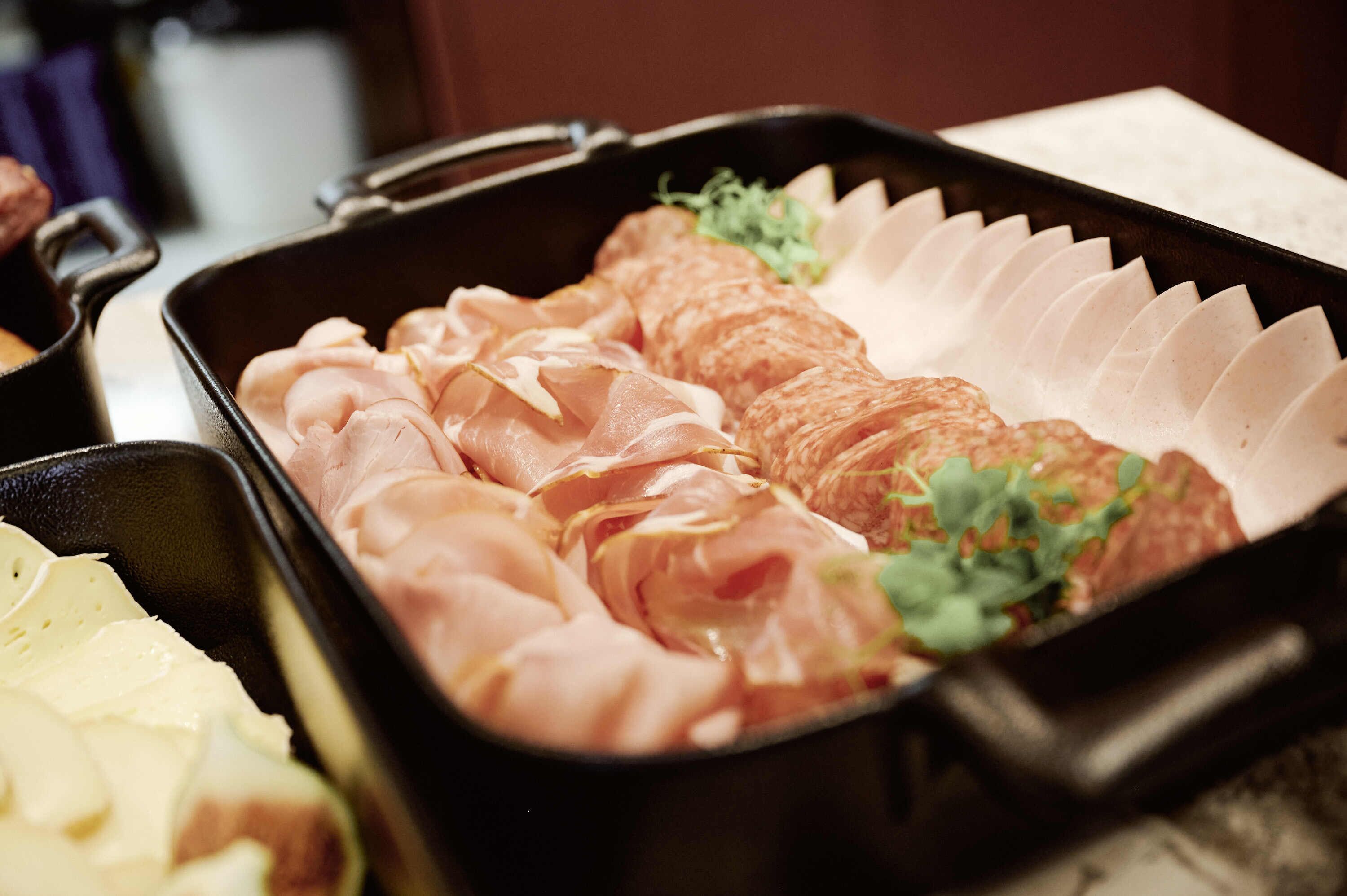 A tray with sliced meats and a small bowl of sauce.