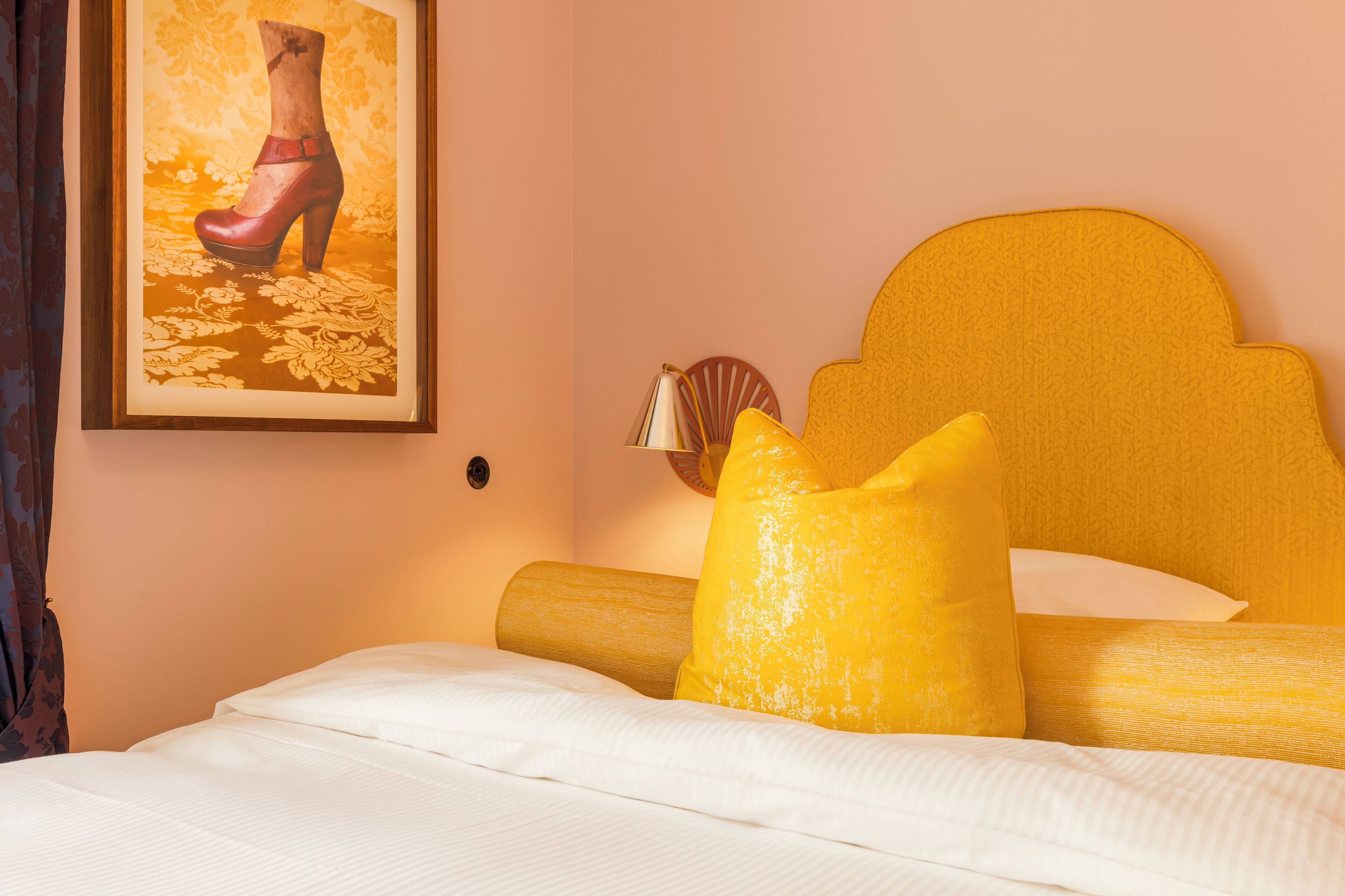 Ein Hotelzimmer mit Bett, Kopfteil, einem gerahmten Bild von einem Schuh und einem Kopfkissen.