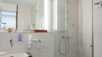 Un baño moderno con ducha envuelta en vidrio, inodoro blanco y lavamanos con espejo sobre él.