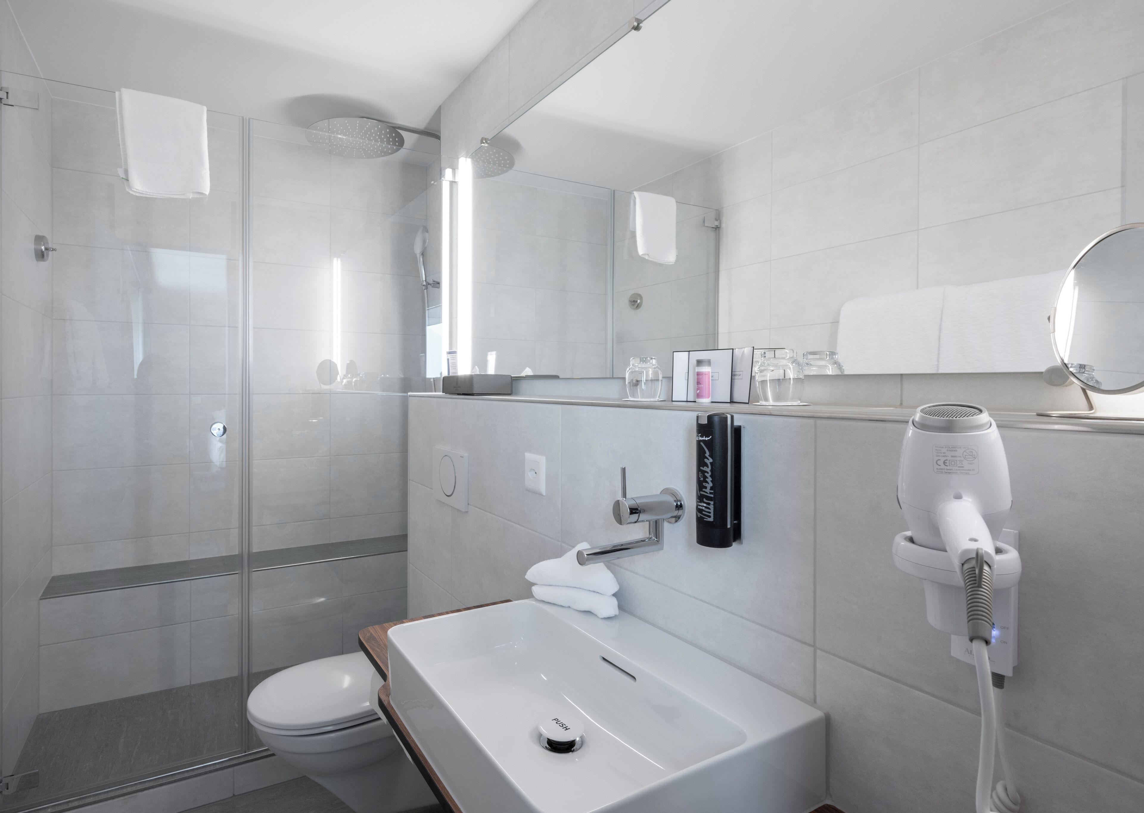 A modern bathroom with a glass shower enclosure, a white sink, and a hairdryer mounted on the wall.