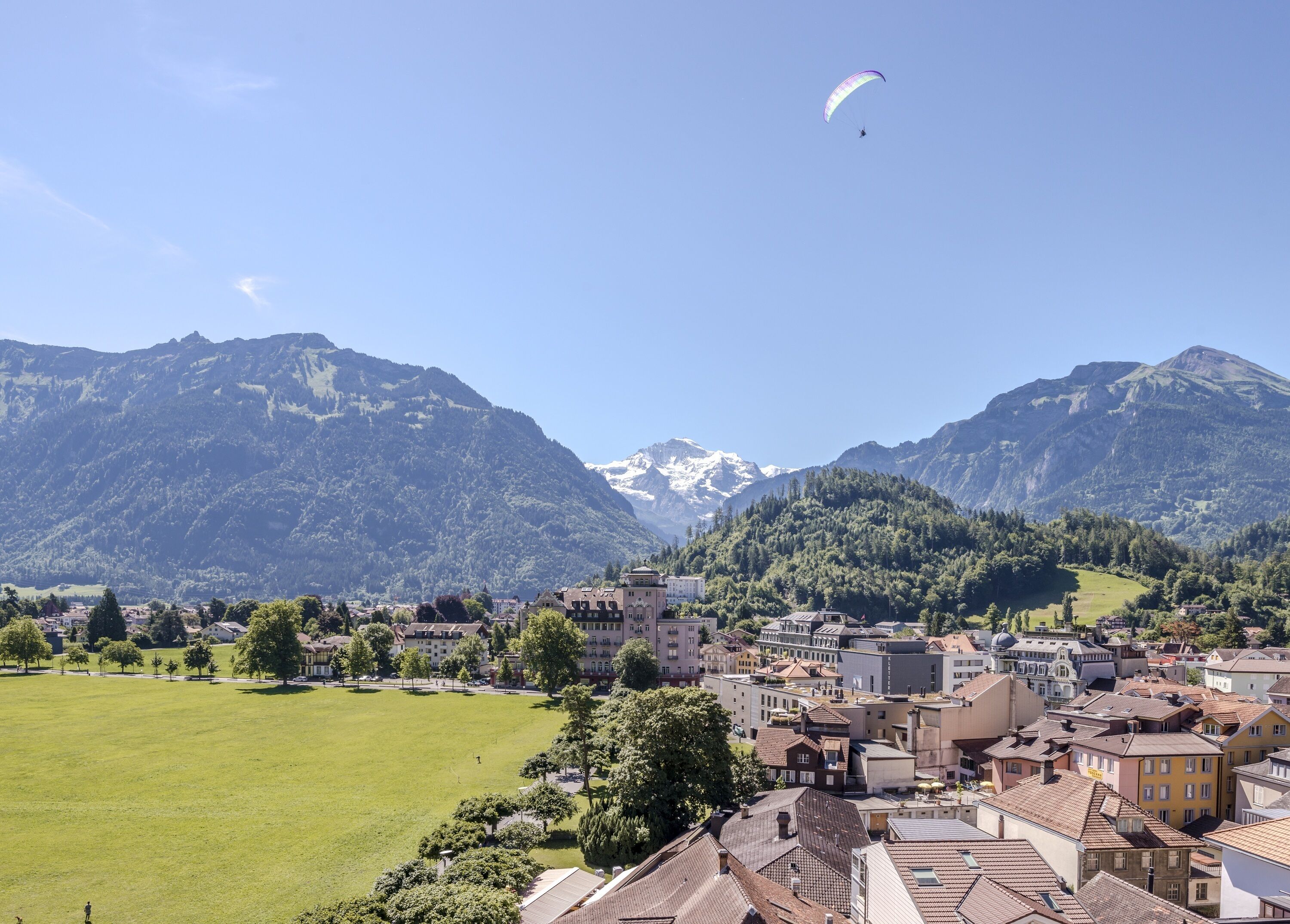 A town with a large open field, buildings, and mountains in the background.
