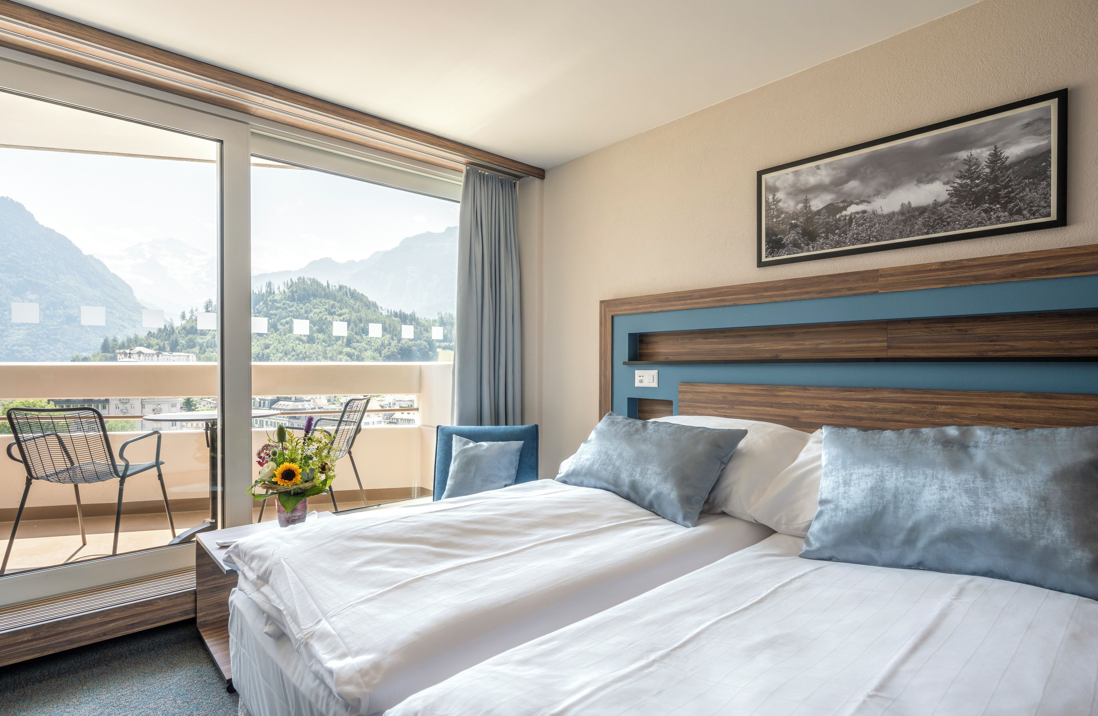 A hotel room with a large bed, a view of mountains, and a balcony with chairs.