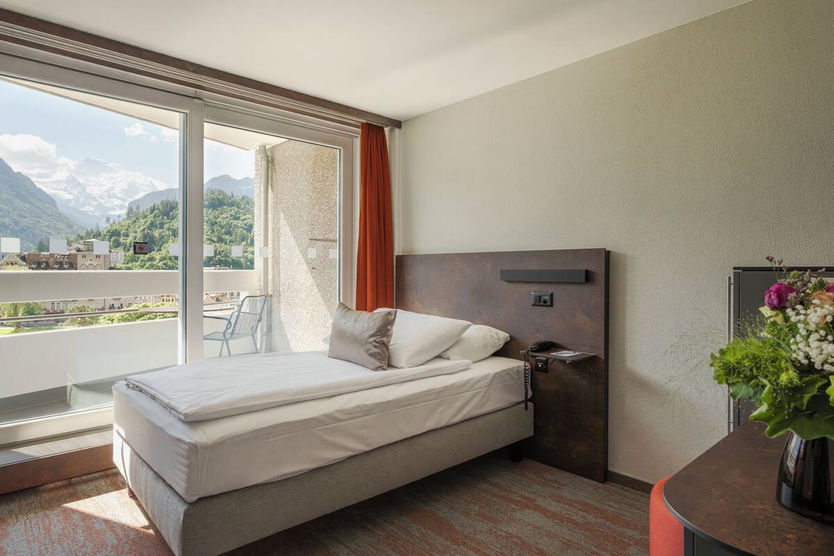 Habitación de hotel con cama, escritorio, teléfono y ventana con vista a las montañas.