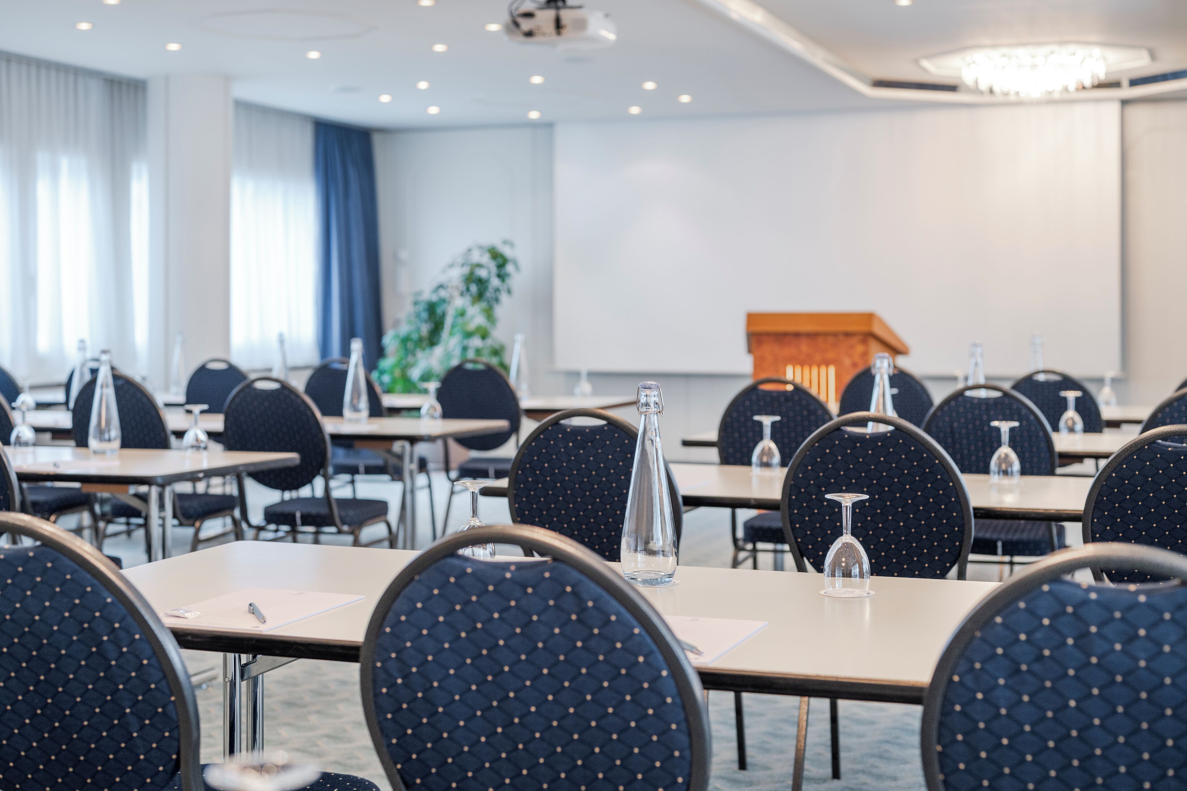 Ein Konferenzraum mit Tischen, Stühlen und einer Projektionsleinwand.