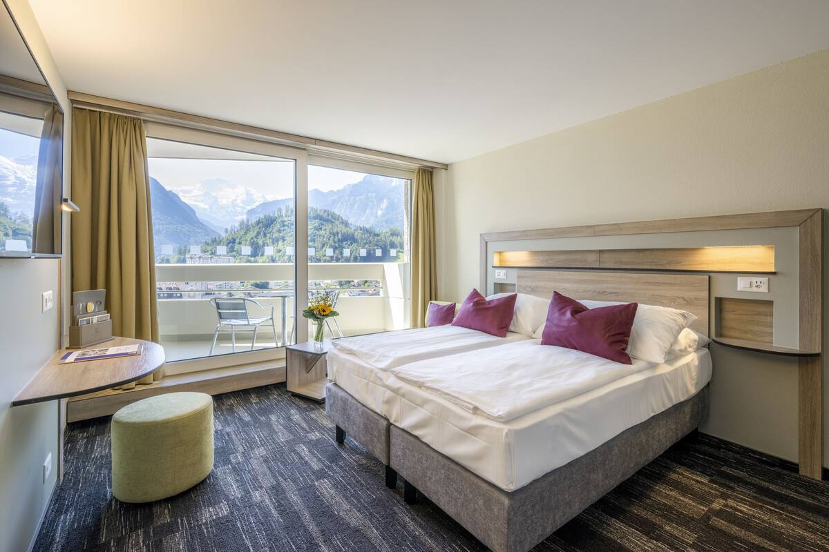 Habitación de hotel con una cama grande, un escritorio, una silla y vistas a las montañas.