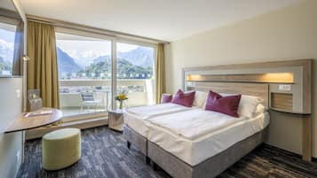 A hotel room with a large bed, a desk, a chair, and a view of mountains.