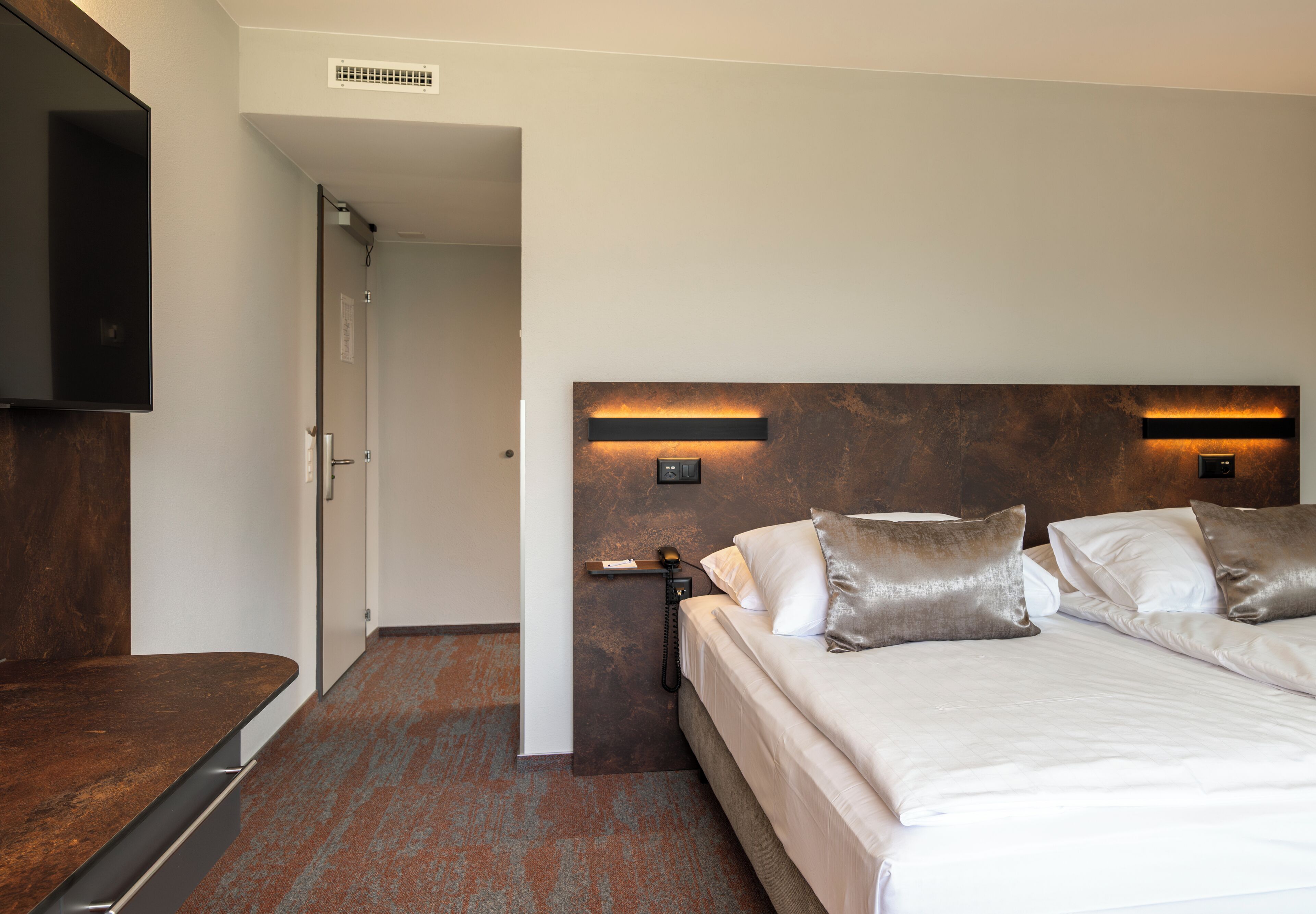 Een hotelkamer met een groot bed, een flatscreen televisie aan de muur en een houten bankje.
