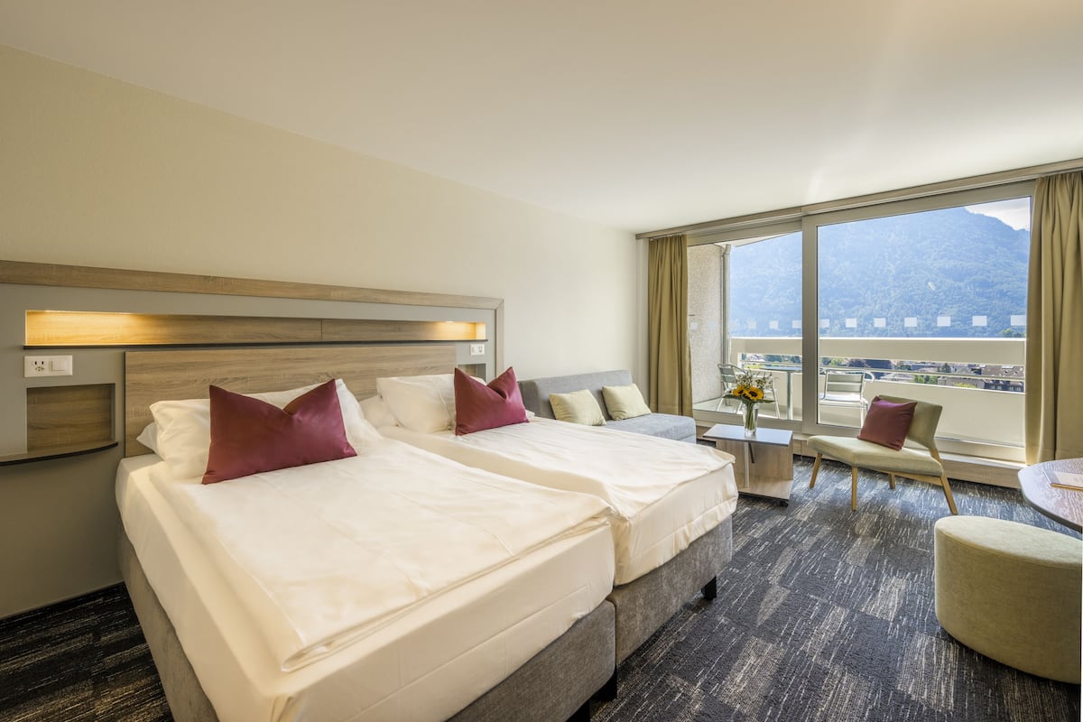 Habitación de hotel con dos camas, un sofá, una mesita y vista a la montaña.