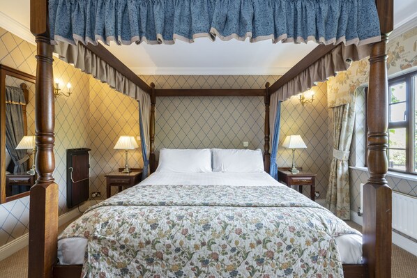 A four-poster bed with a floral bedspread, two bedside tables with lamps, a mirror, and a window with curtains. - Abbeyglen Castle Hotel (Clifden)