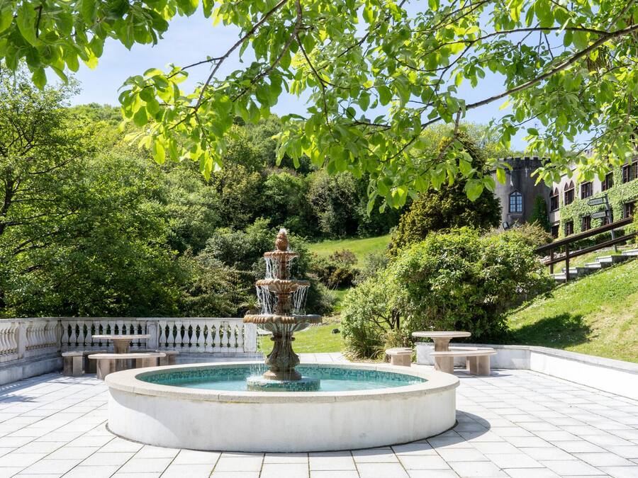 A circular fountain with multiple tiers, surrounded by a white tiled patio with benches.