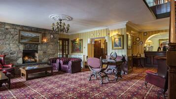 A traditional room with a stone fireplace, leather furniture, patterned carpet, and a chandelier.
