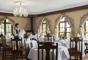 A restaurant with multiple tables set for dining, a chandelier, and large windows with curtains. - Abbeyglen Castle Hotel (Clifden)