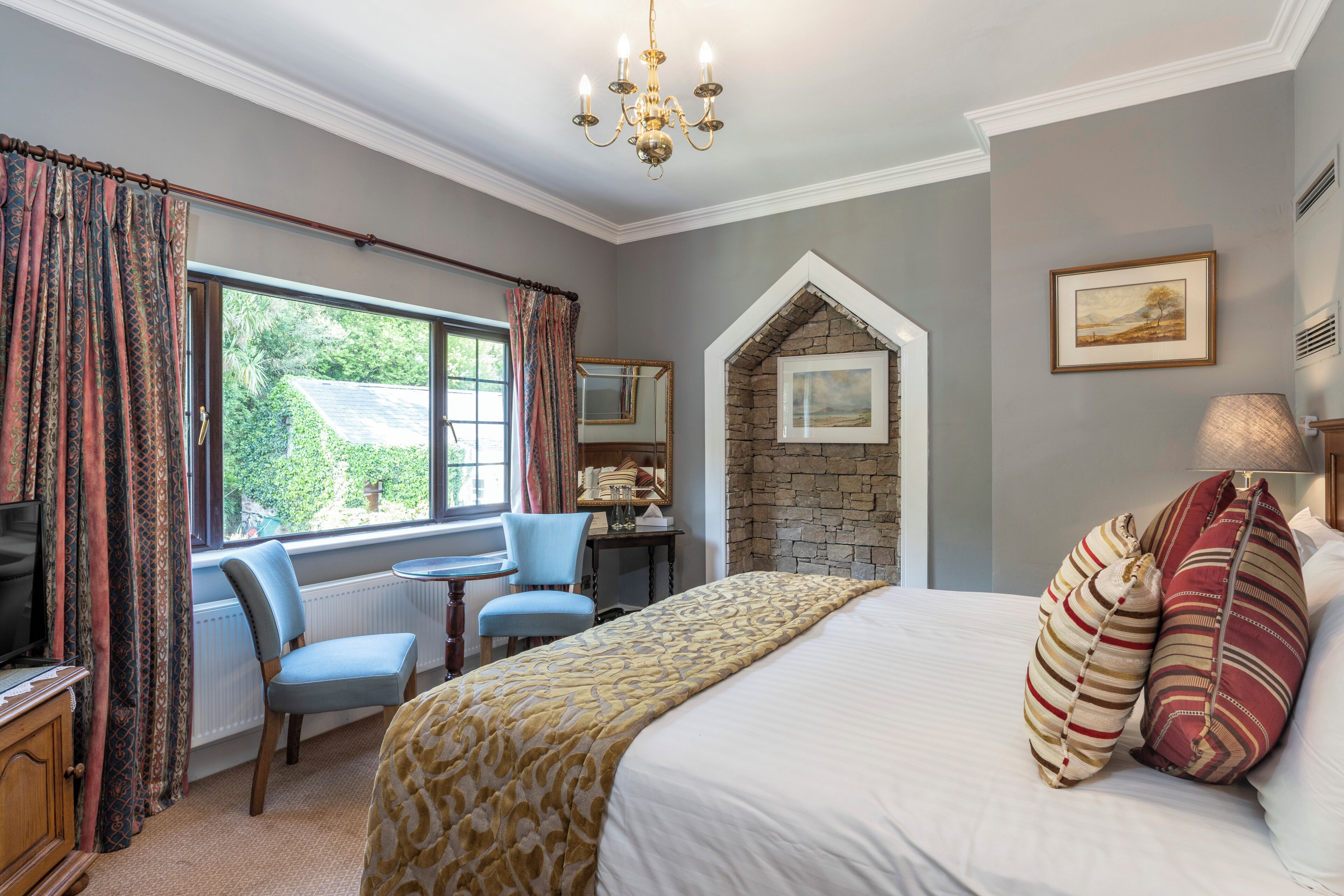 A bedroom with a bed, a desk, a chair, a television, and a window with curtains.