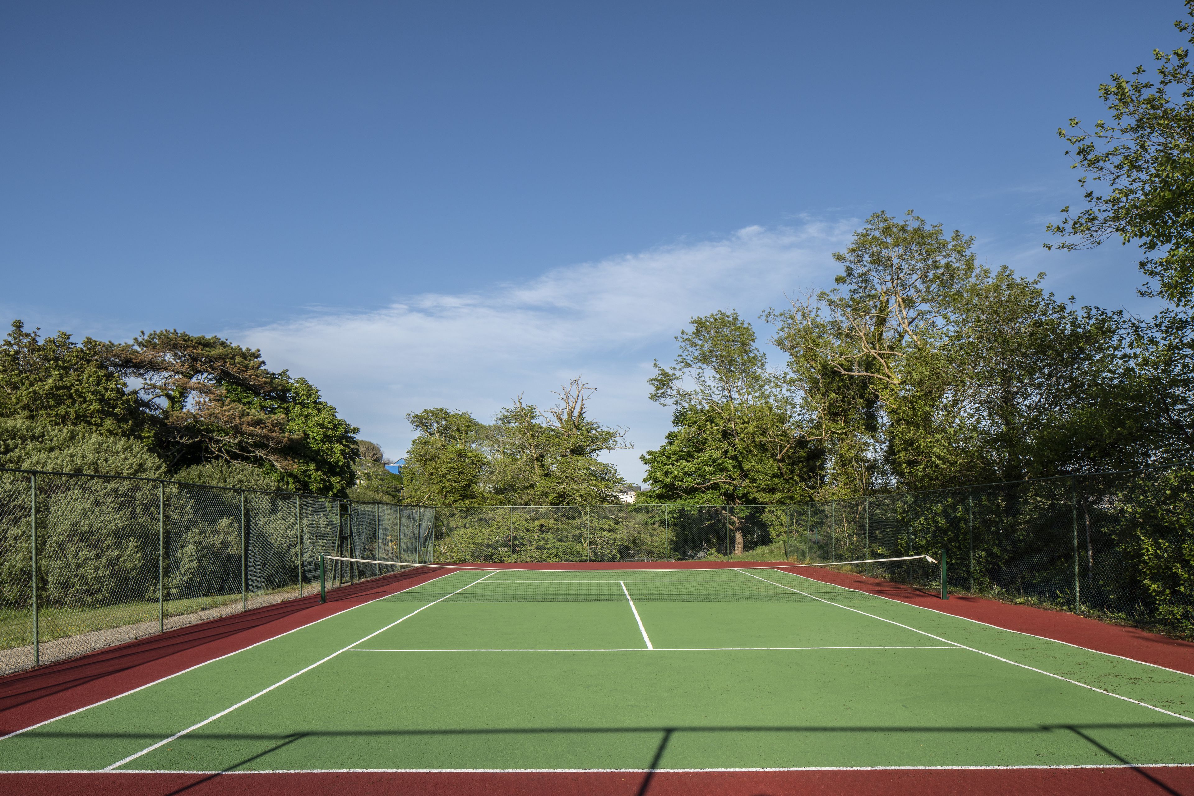 Una cancha de tenis con red, rodeada de árboles y una valla.