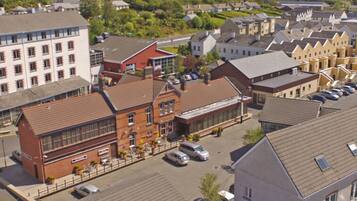 Vue aérienne d’un ensemble de bâtiments comprenant plusieurs structures, notamment un imposant bâtiment en briques rouges doté de grandes fenêtres et d’un toit plat, situé à côté d’un bâtiment blanc présentant un style architectural similaire.