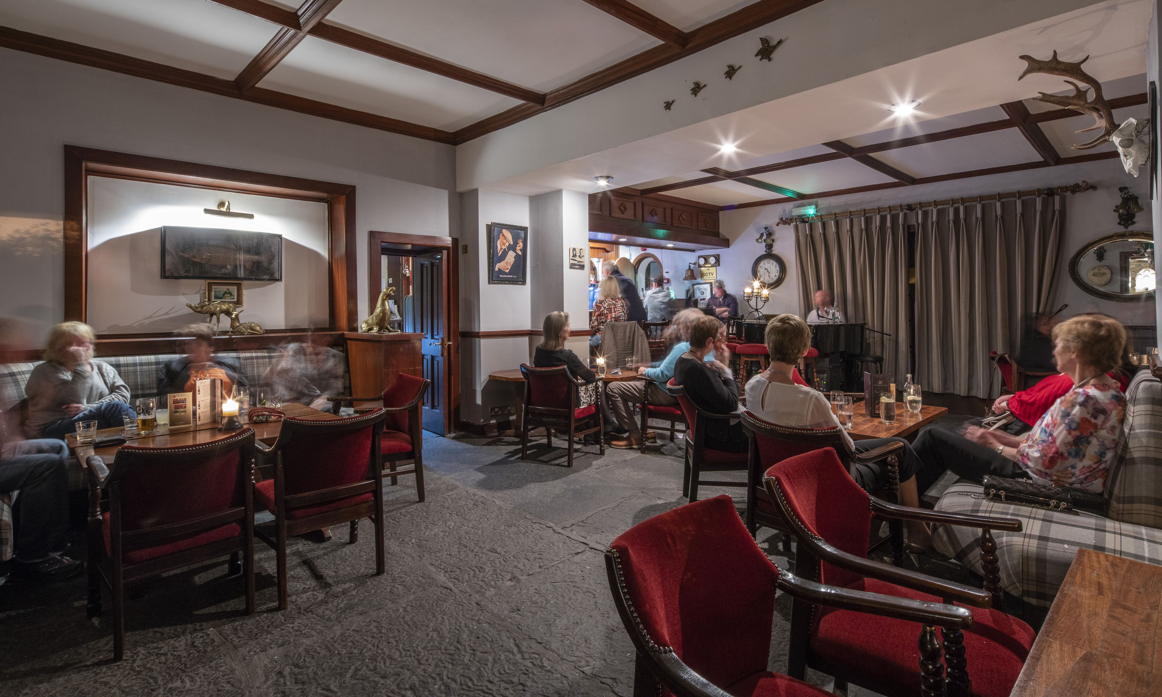 Ein gemütliches Restaurant mit Holzbalken, rot gepolsterten Stühlen und einem Klavier im Hintergrund.