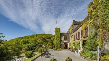 A historic building with ivy-covered walls, a central tower, and a paved courtyard with outdoor seating.