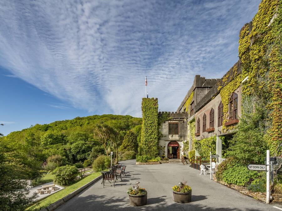 A historic building with ivy-covered walls, a central tower, and a paved courtyard with outdoor seating.