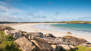 A coastal beach with large rocks in the foreground, a sandy shoreline, and a clear blue sky. - Abbeyglen Castle Hotel (Clifden)