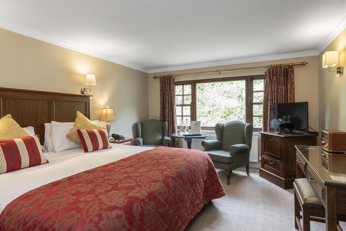 Une chambre d’hôtel avec un grand lit, un bureau, une chaise, une télévision et une fenêtre avec des rideaux.