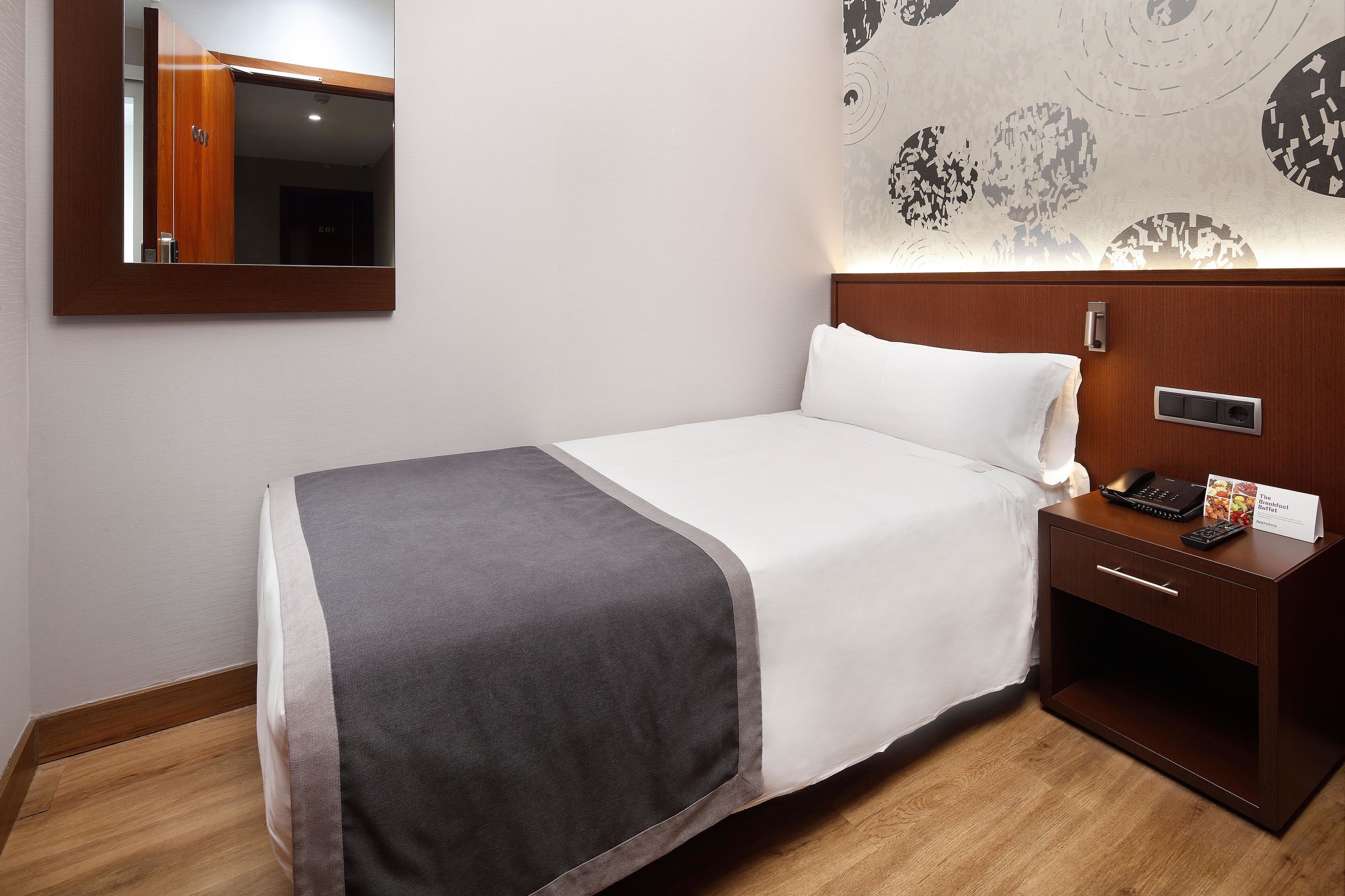 A hotel room with a bed, bedside table, and a mirror.