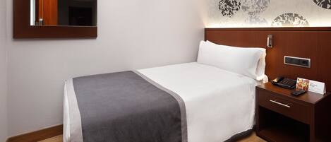 A hotel room with a bed, bedside table, and a mirror.