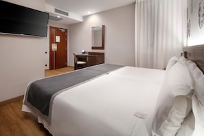 A hotel room with a large bed, a desk with a chair, a flat-screen TV mounted on the wall, and a mirror above the desk. - Hotel HCC Taber (Barcelona)